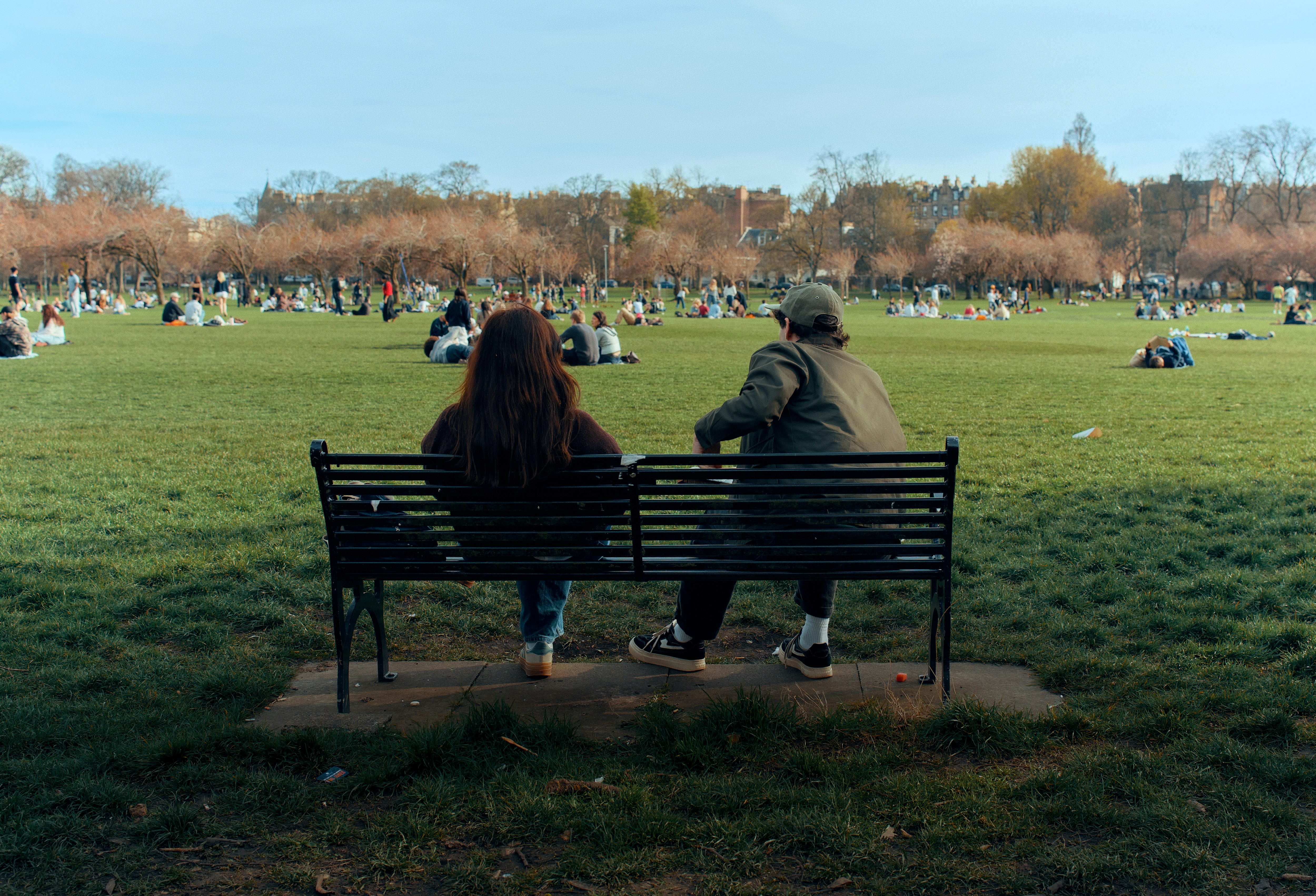 Two people sit on a park bench watching others.