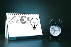 Desk calendar with business symbols and alarm clock.