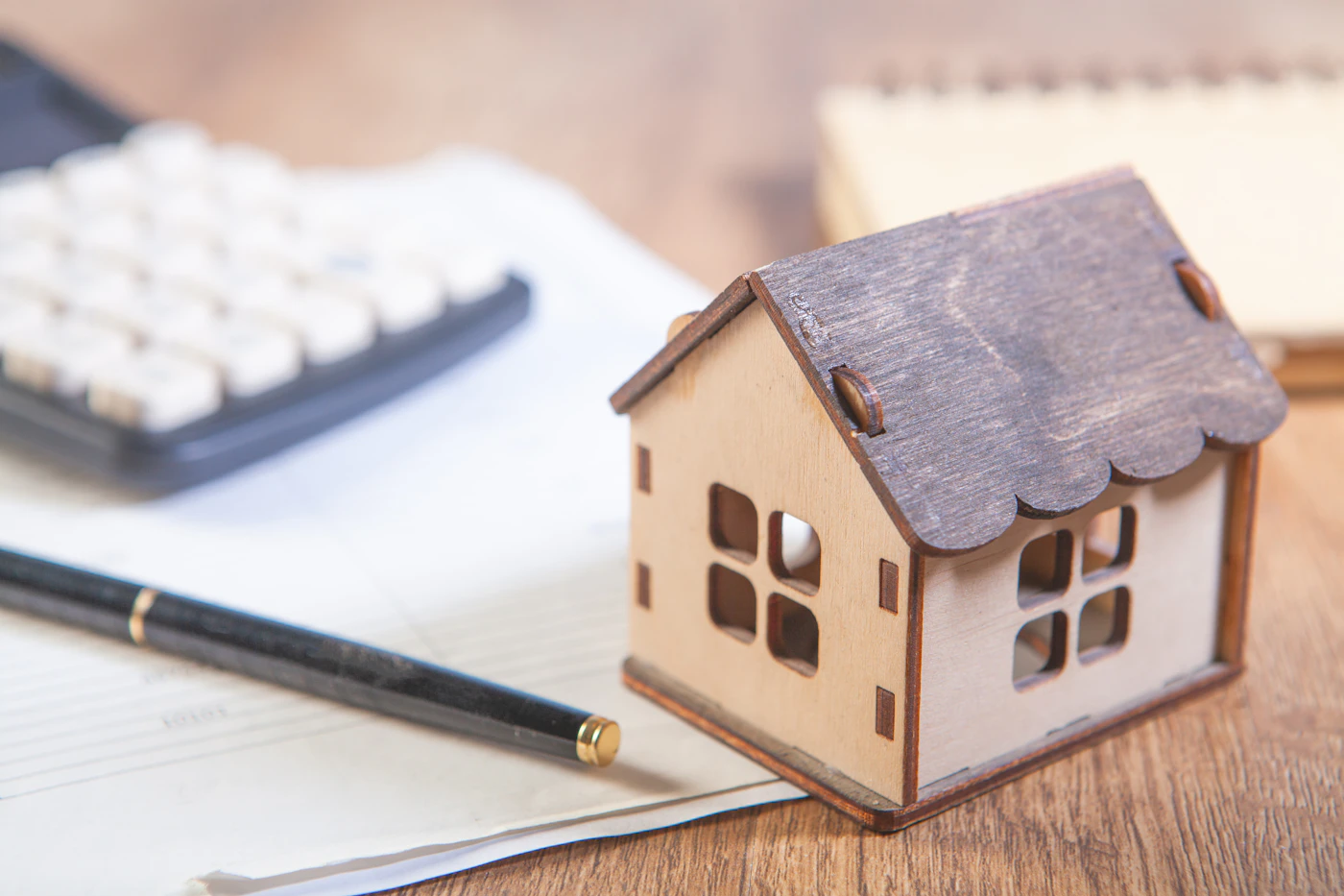 Maquette de maison en bois sur un bureau avec calculatrice, carnet et stylo
