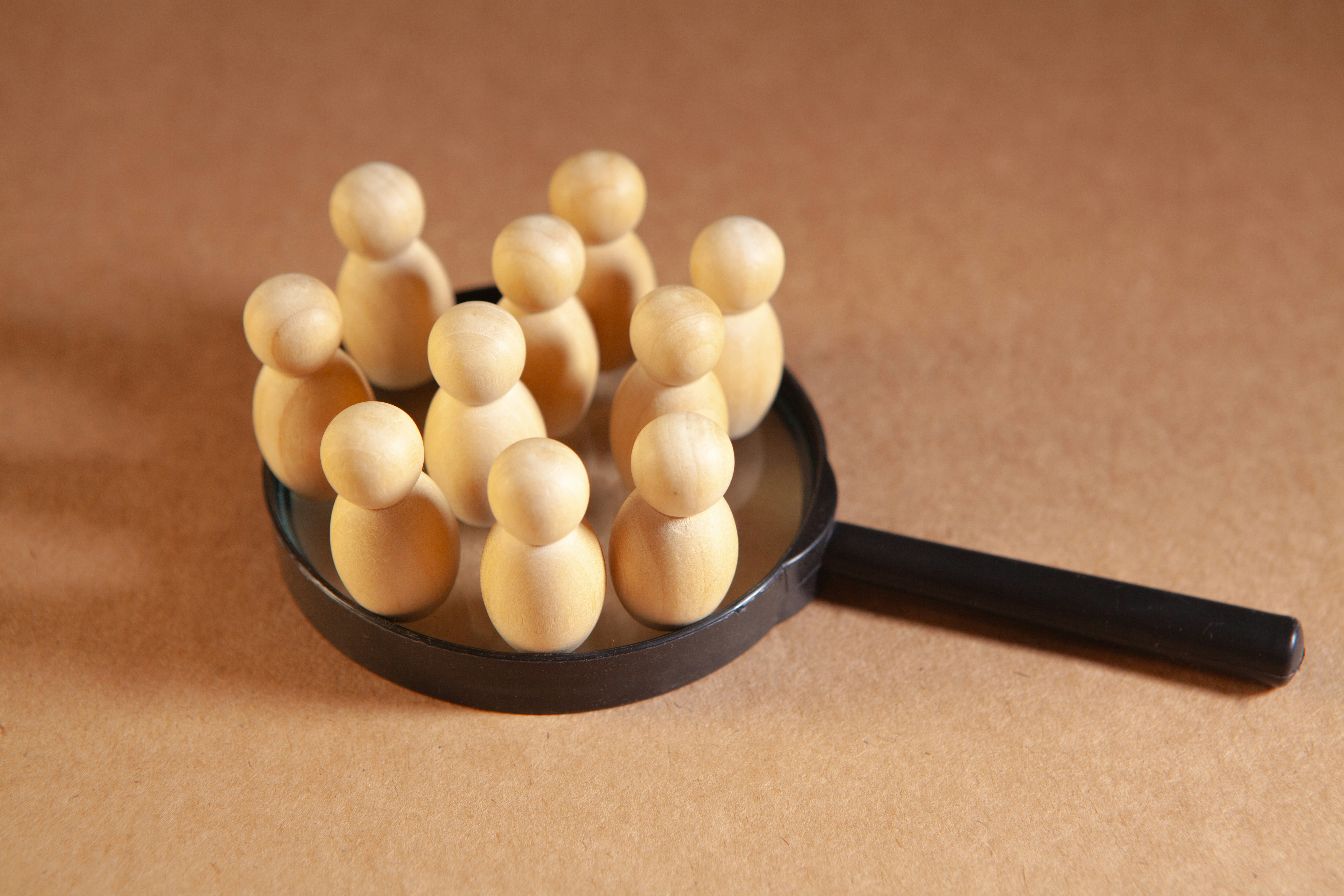 Wooden figures clustered on a magnifying glass.