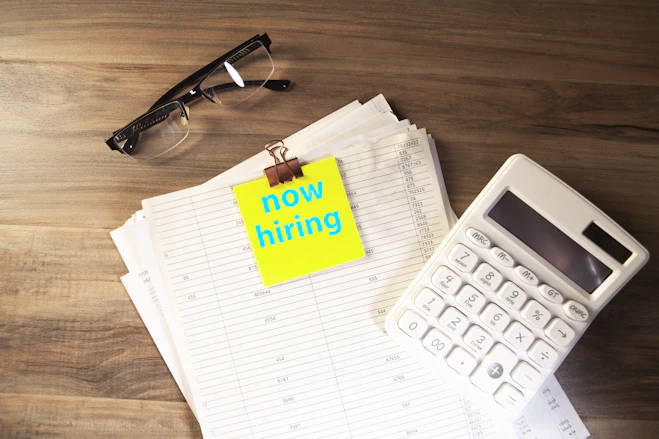 Calculator, glasses, and papers with 'now hiring' note