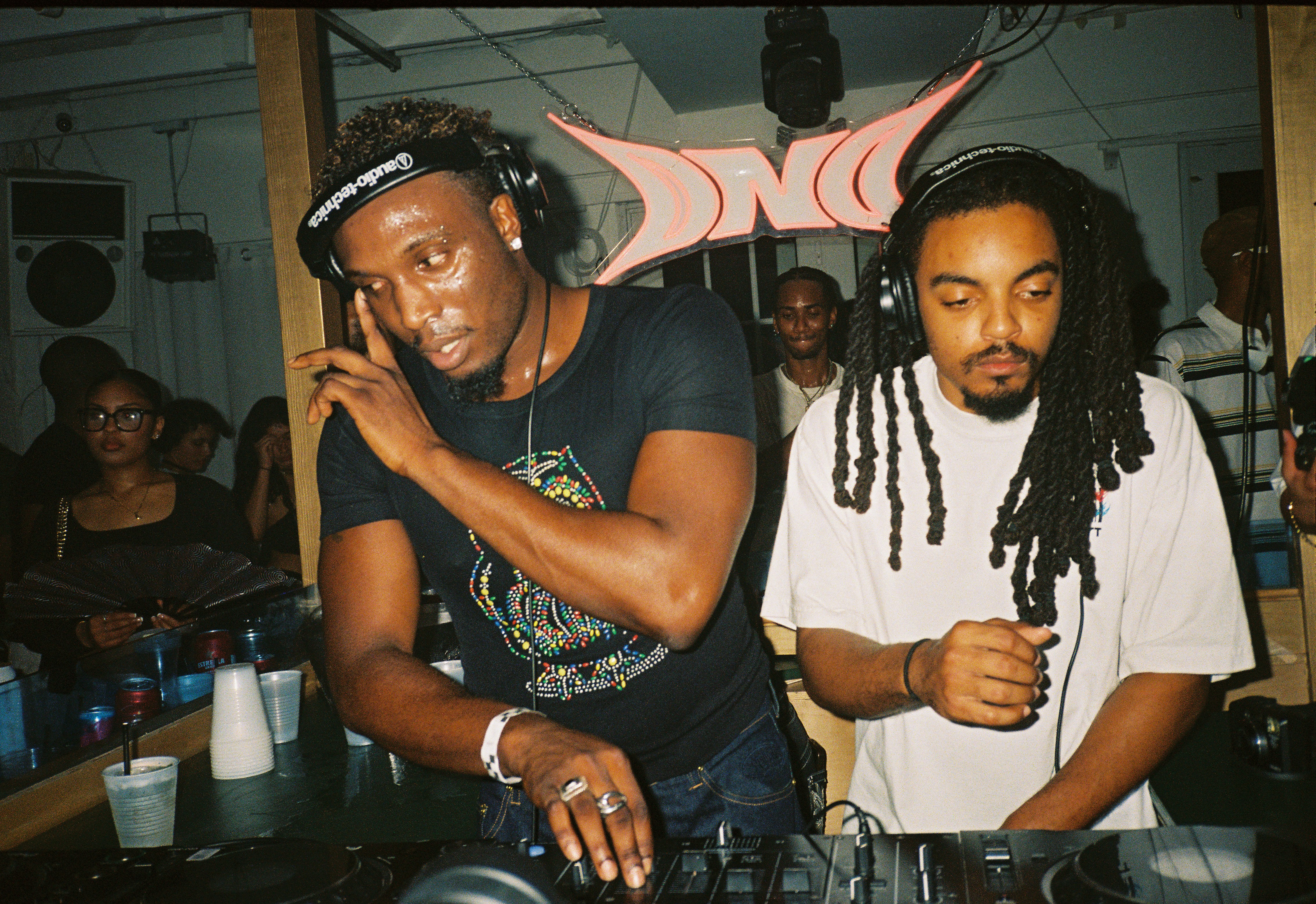 Two djs performing at a party with a crowd.