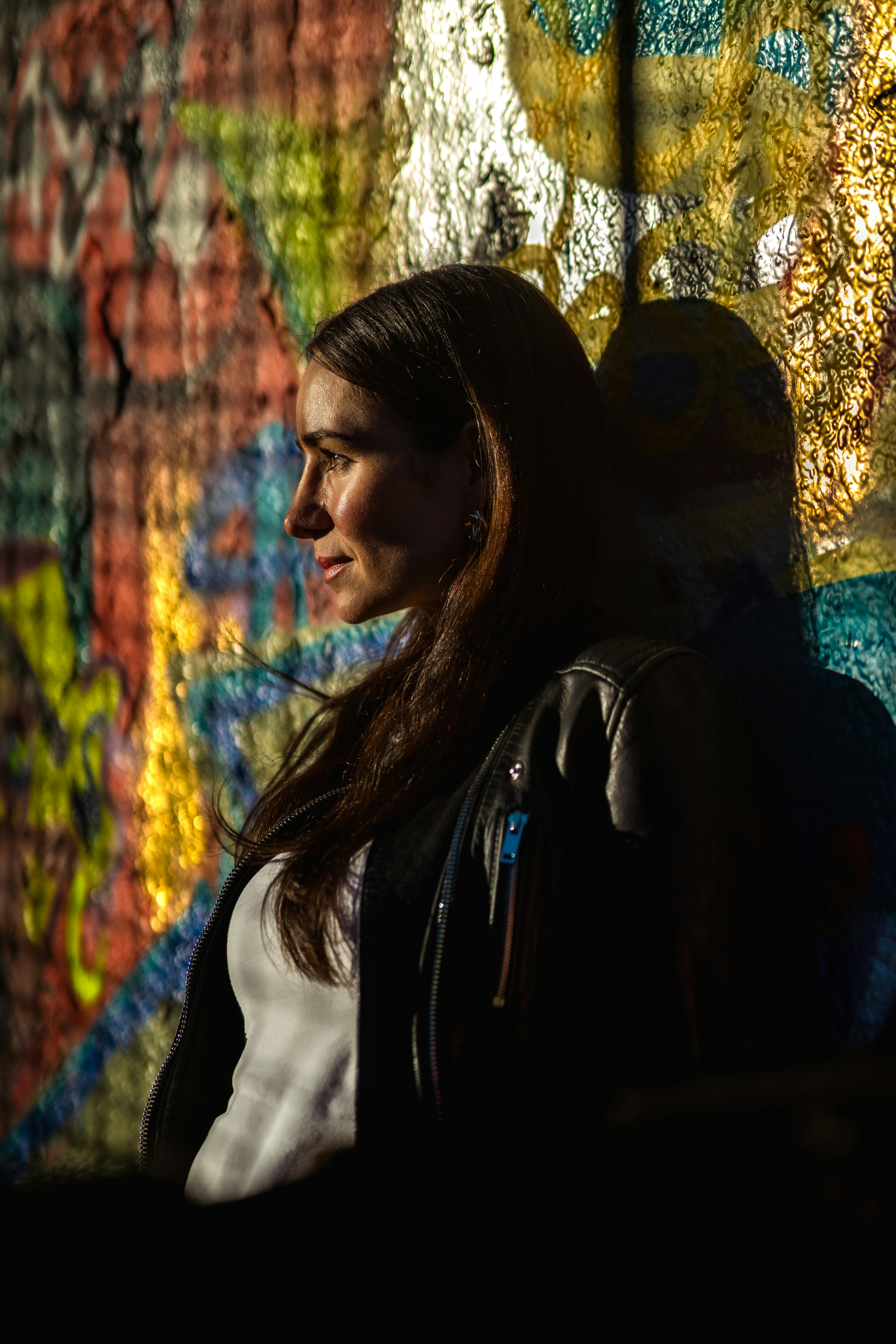 Donna appoggiata al muro dei graffiti con un'illuminazione drammatica.