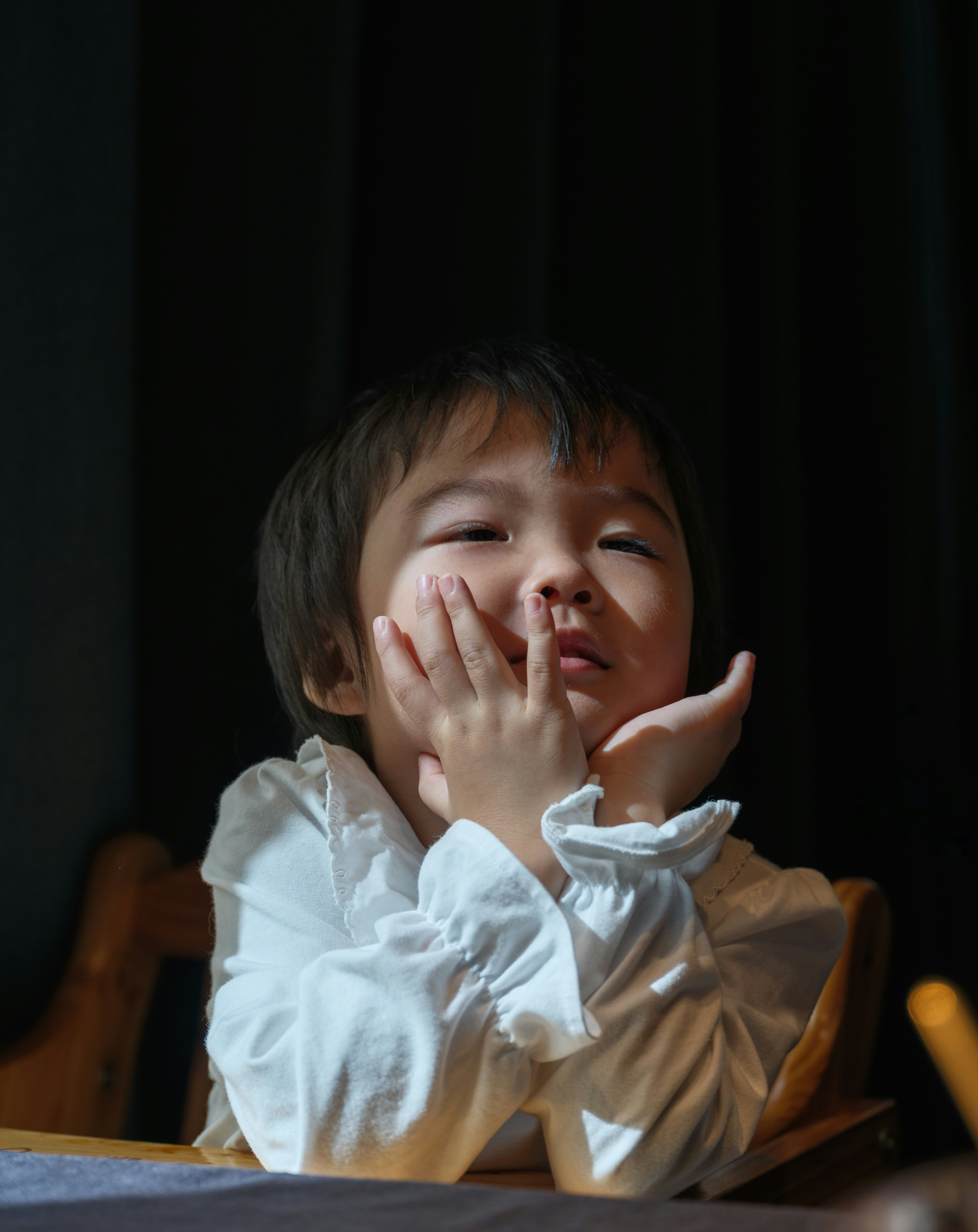 Ein kleines Kind mit der Hand am Kinn, das nach oben schaut.