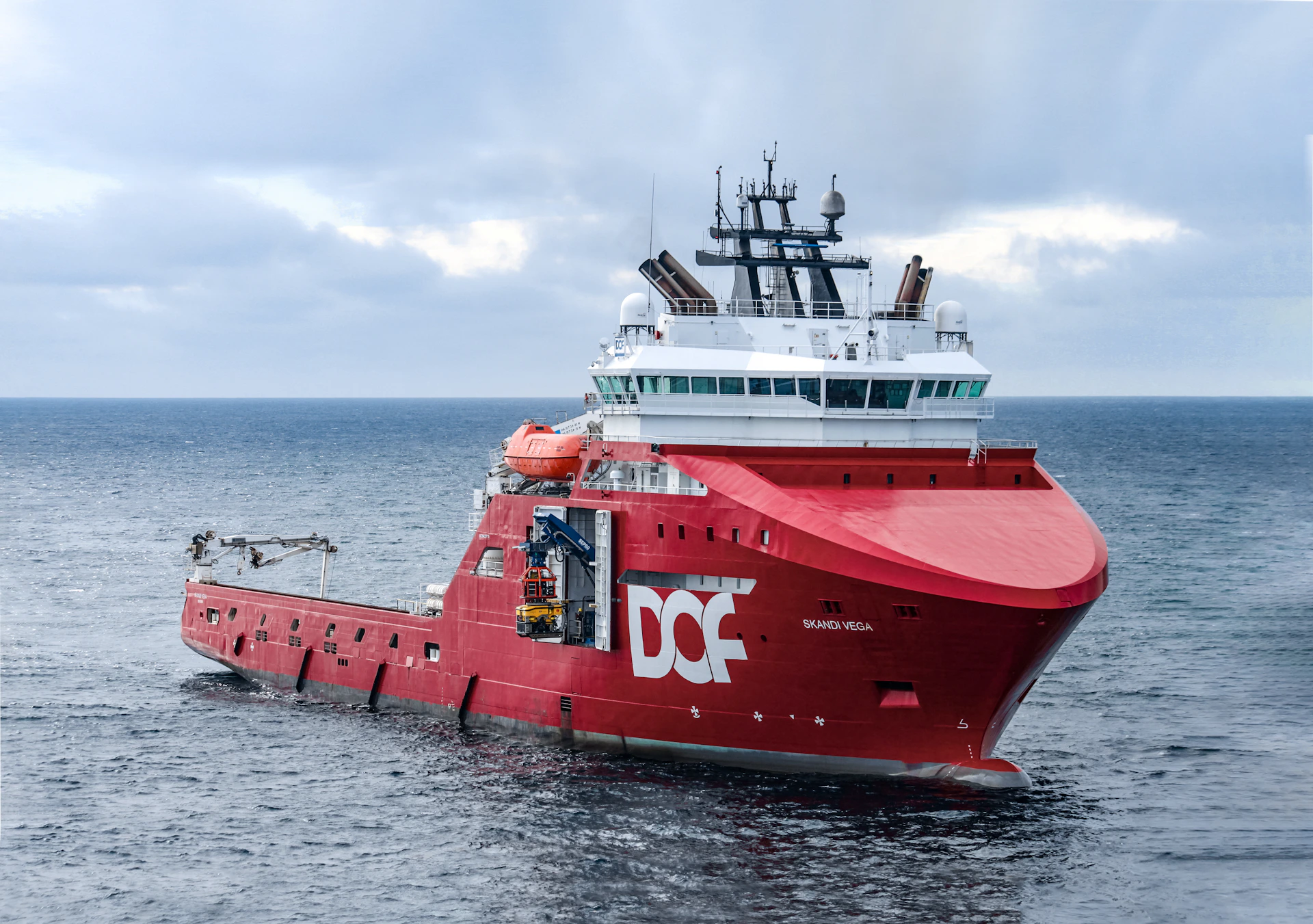 A red offshore supply vessel sailing on the ocean