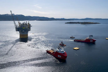 Oil rig platform being towed by support vessels at sea
