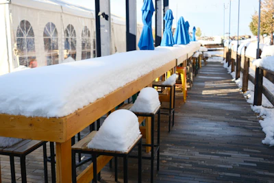 Long outdoor bar covered in snow with blue umbrellas.