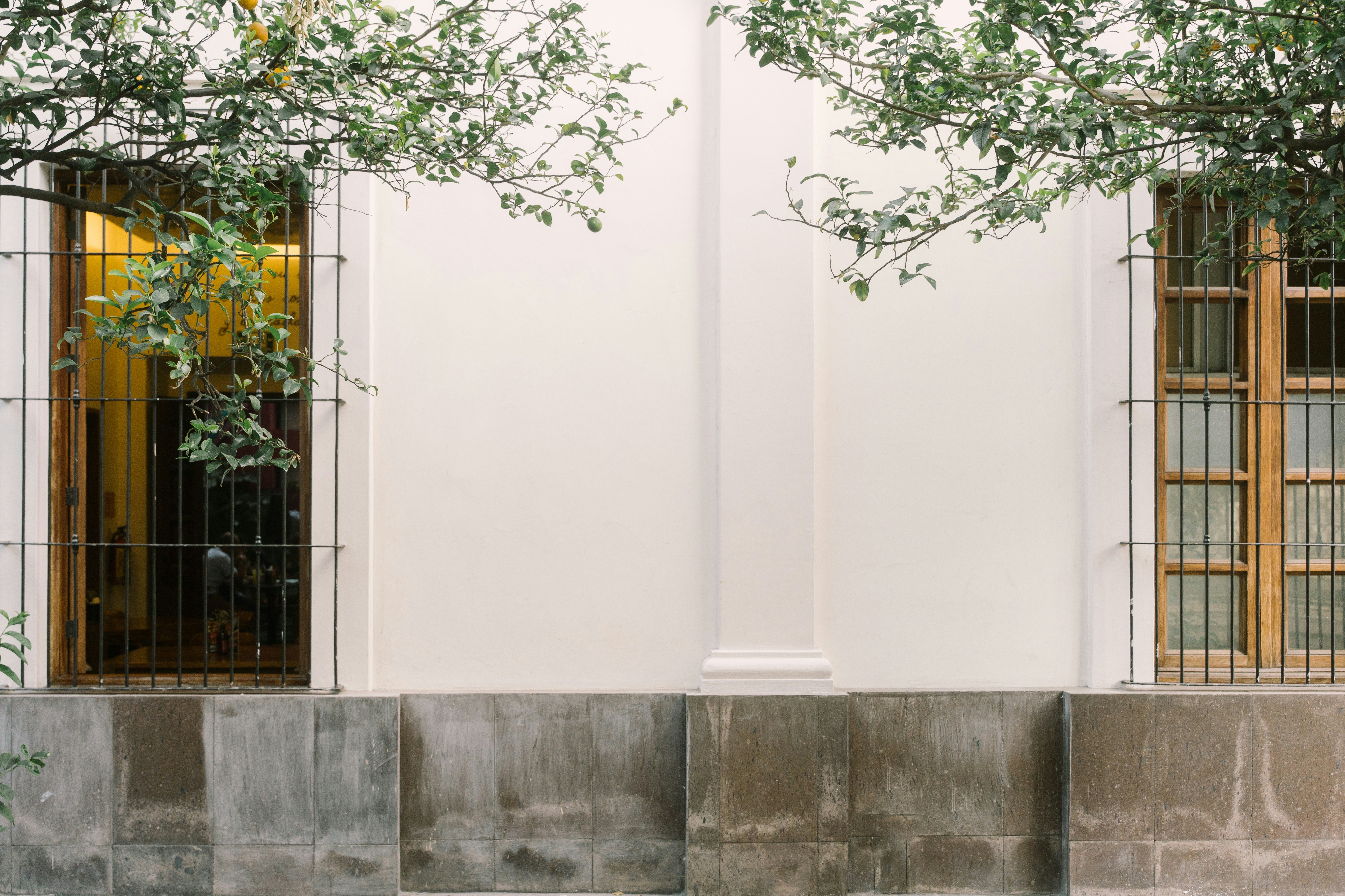 Weiße Gebäudefassade mit zwei Fenstern und Betonsockel.