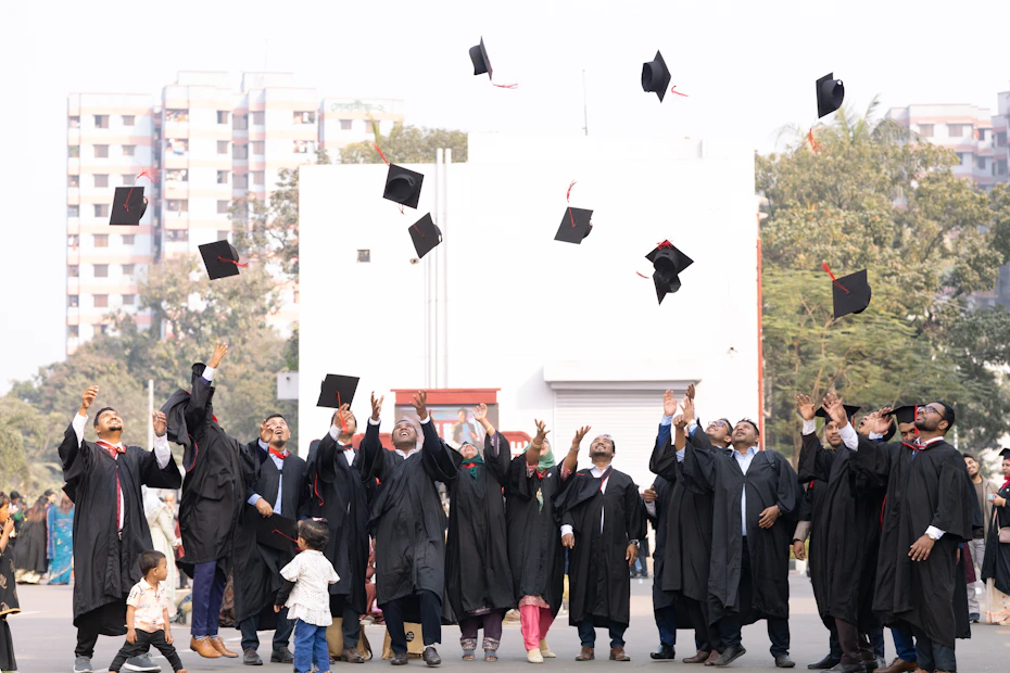 Graduates in caps and gowns toss hats in the air.