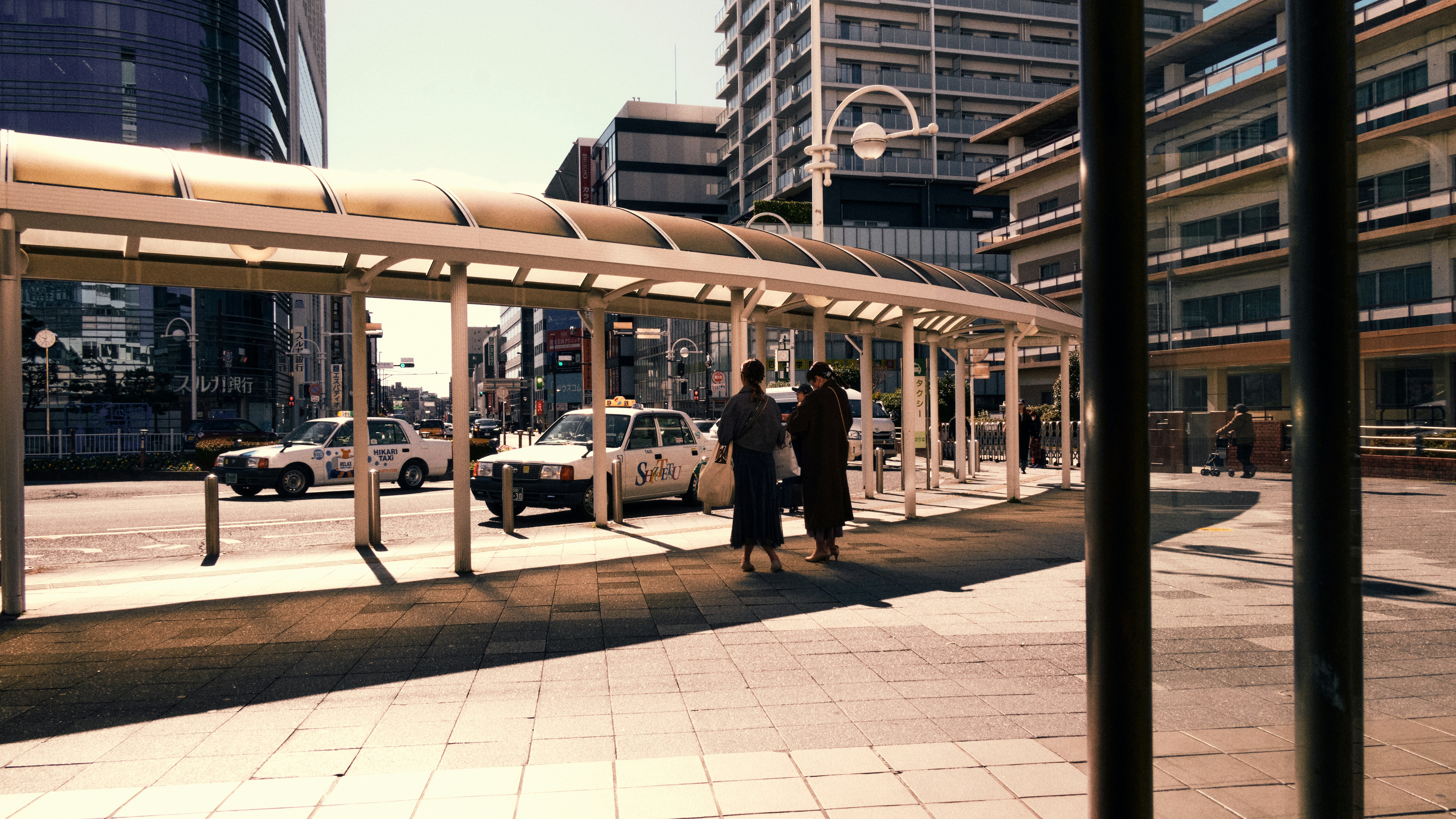 People waiting at a covered bus stop with taxis nearby.