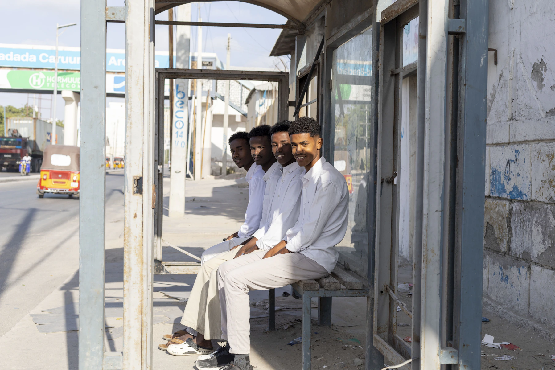 Four men sit at a bus stop in white shirts.