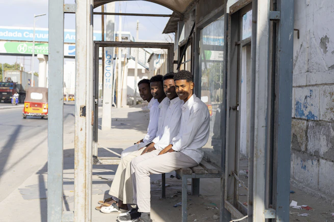 Four men sit at a bus stop in white shirts.