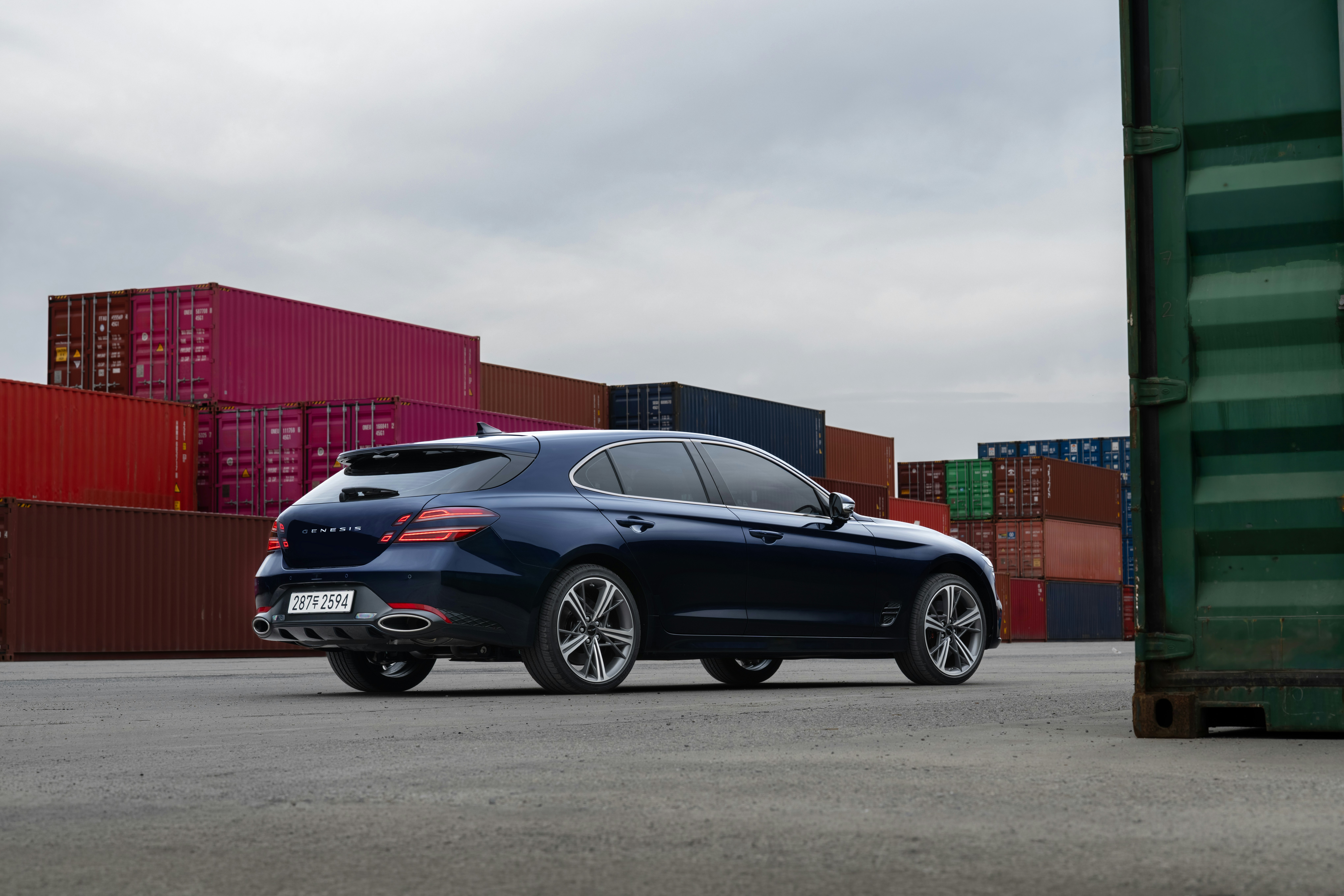 A dark blue car parked among shipping containers
