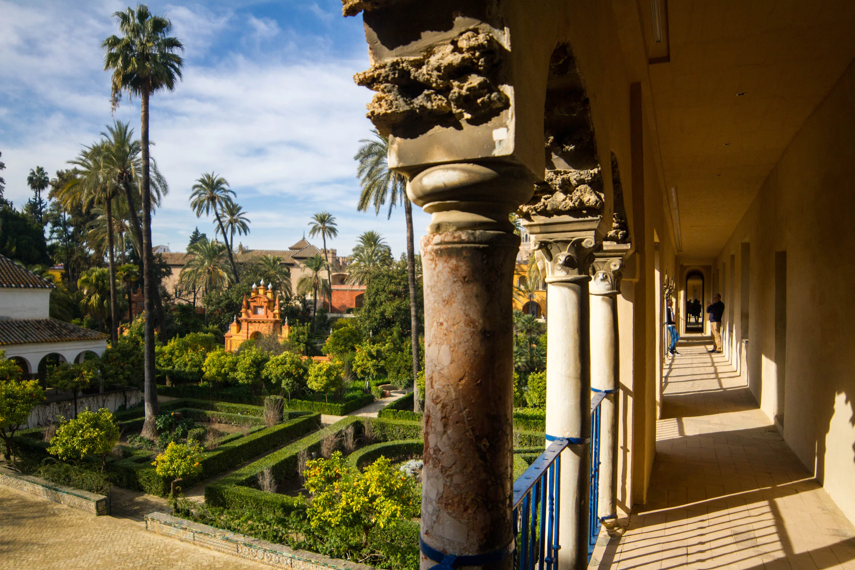 A shaded colonnade, fountain and palm-filled garden inside Seville's Real Alcázar
