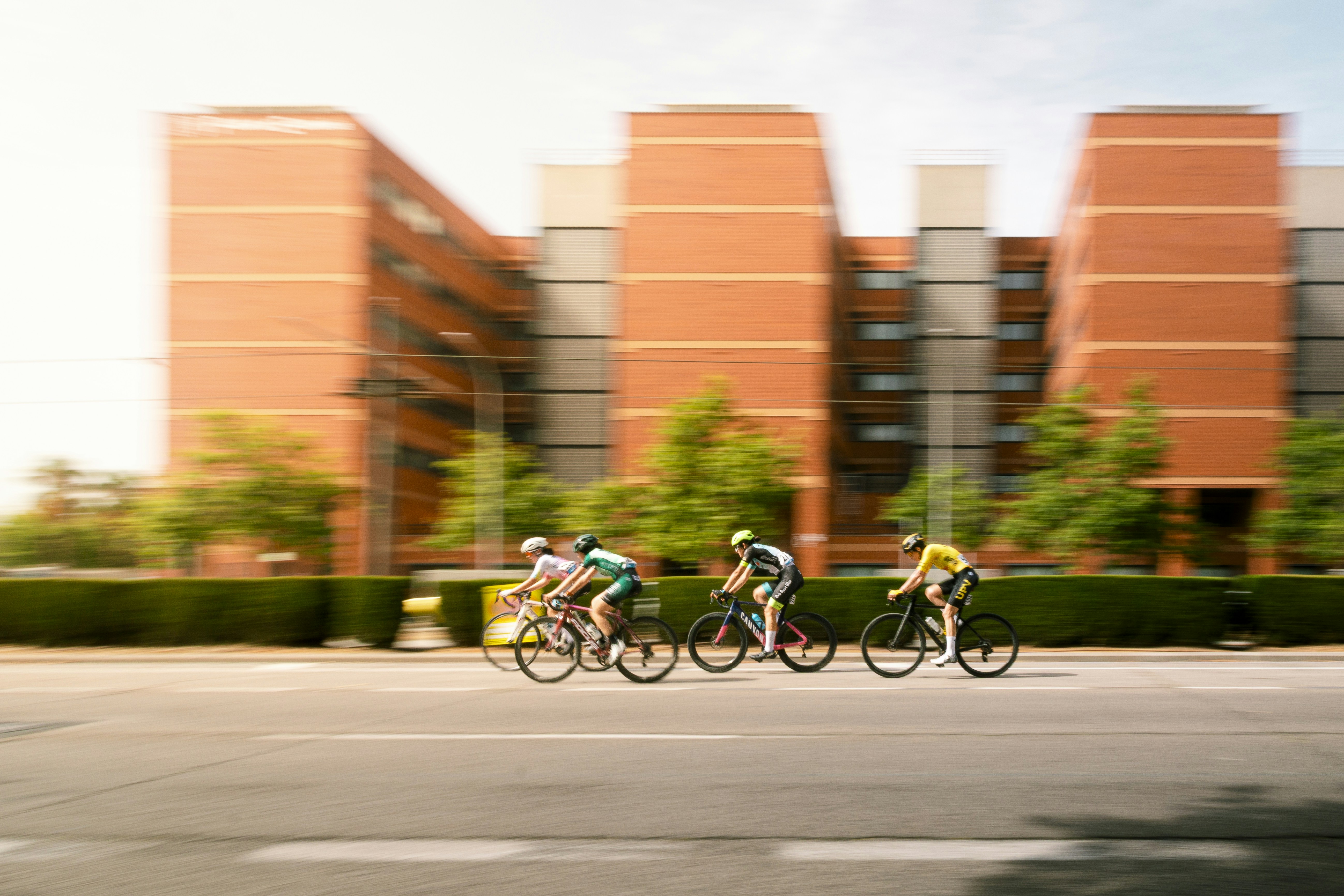 Cyclists racing in front of a modern brick building.