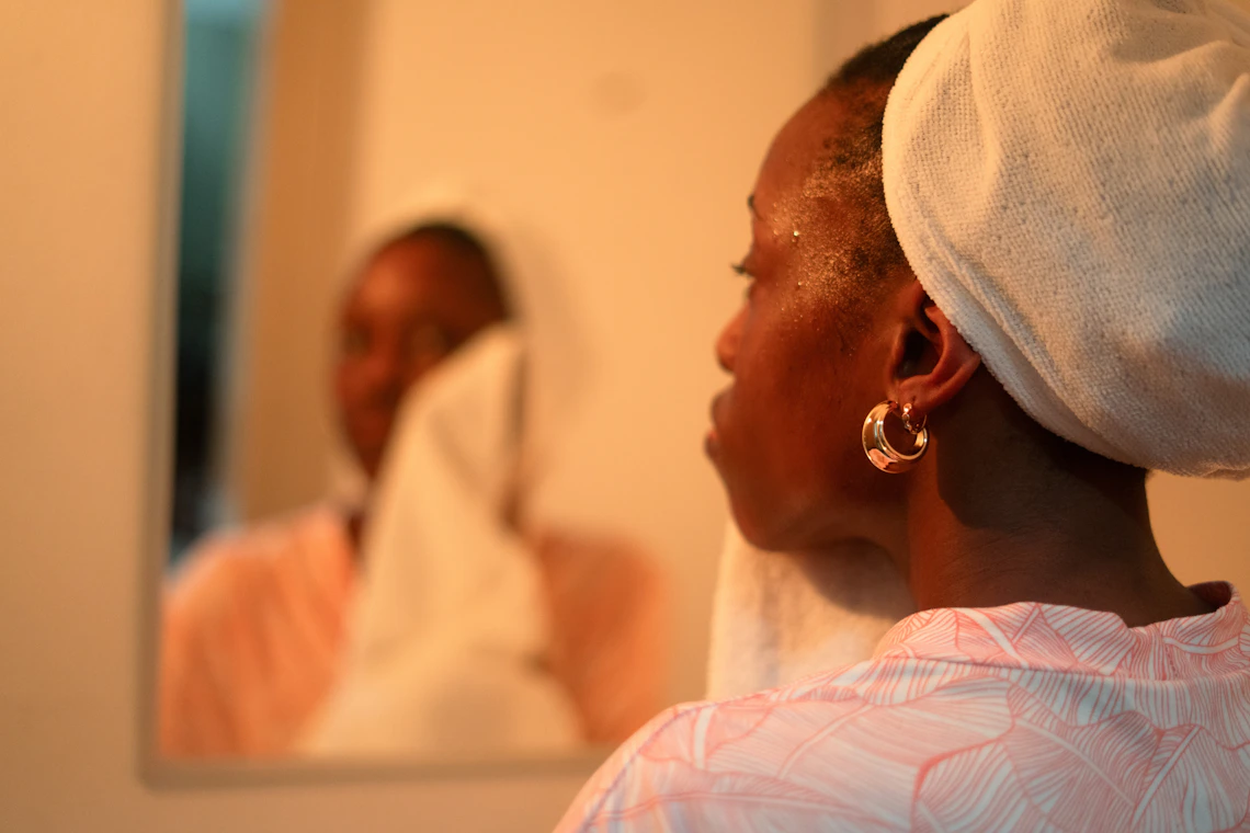 Woman completing a gentle facial cleansing routine in front of a mirror
