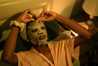A woman applies a sheet mask in bed.