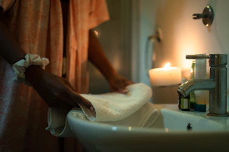Woman folding a towel by a sink with candle.