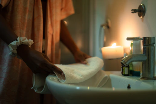 Woman folding a towel by a sink with candle.