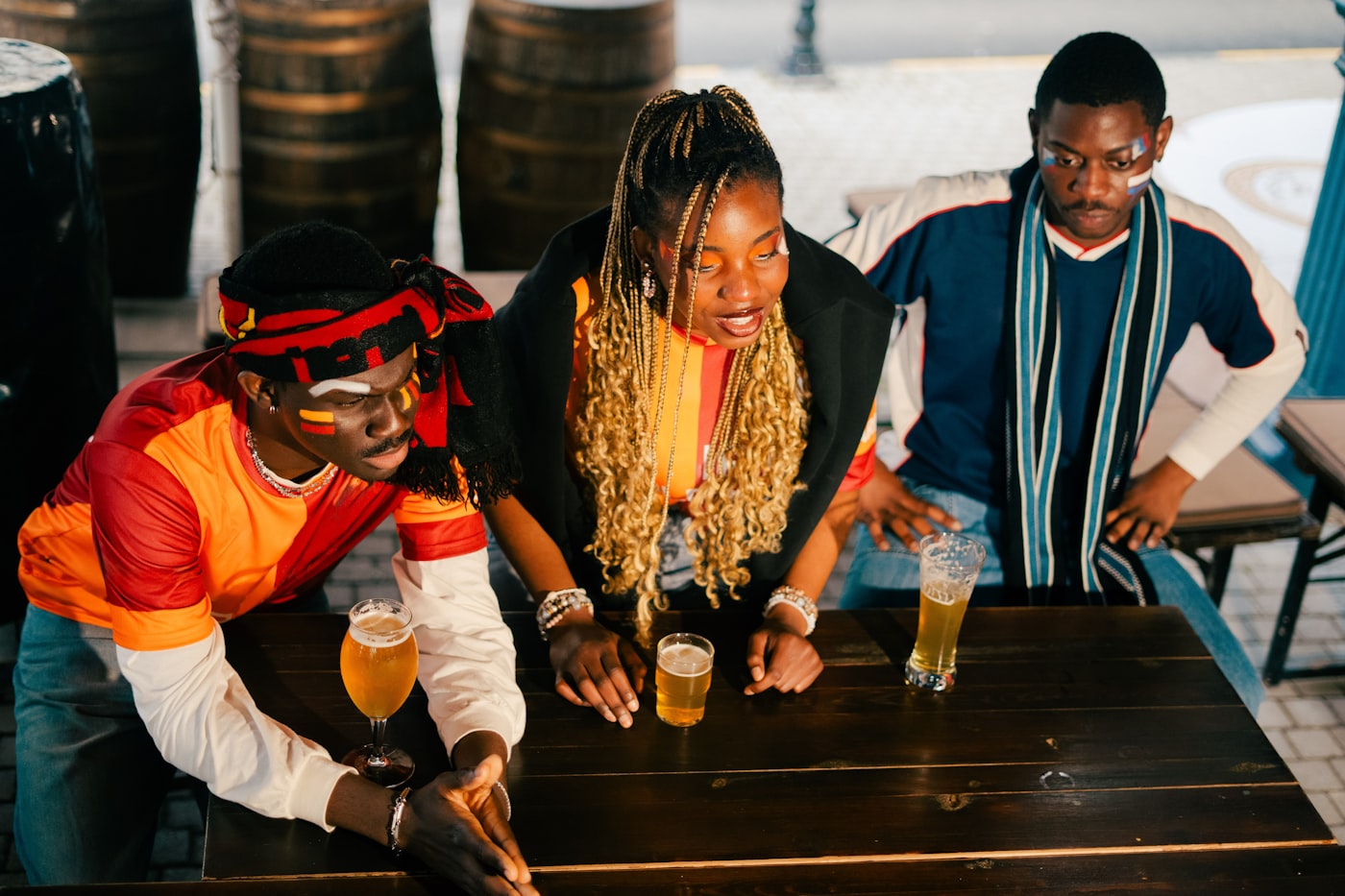Three fans in jerseys and face paint watching the match with beers