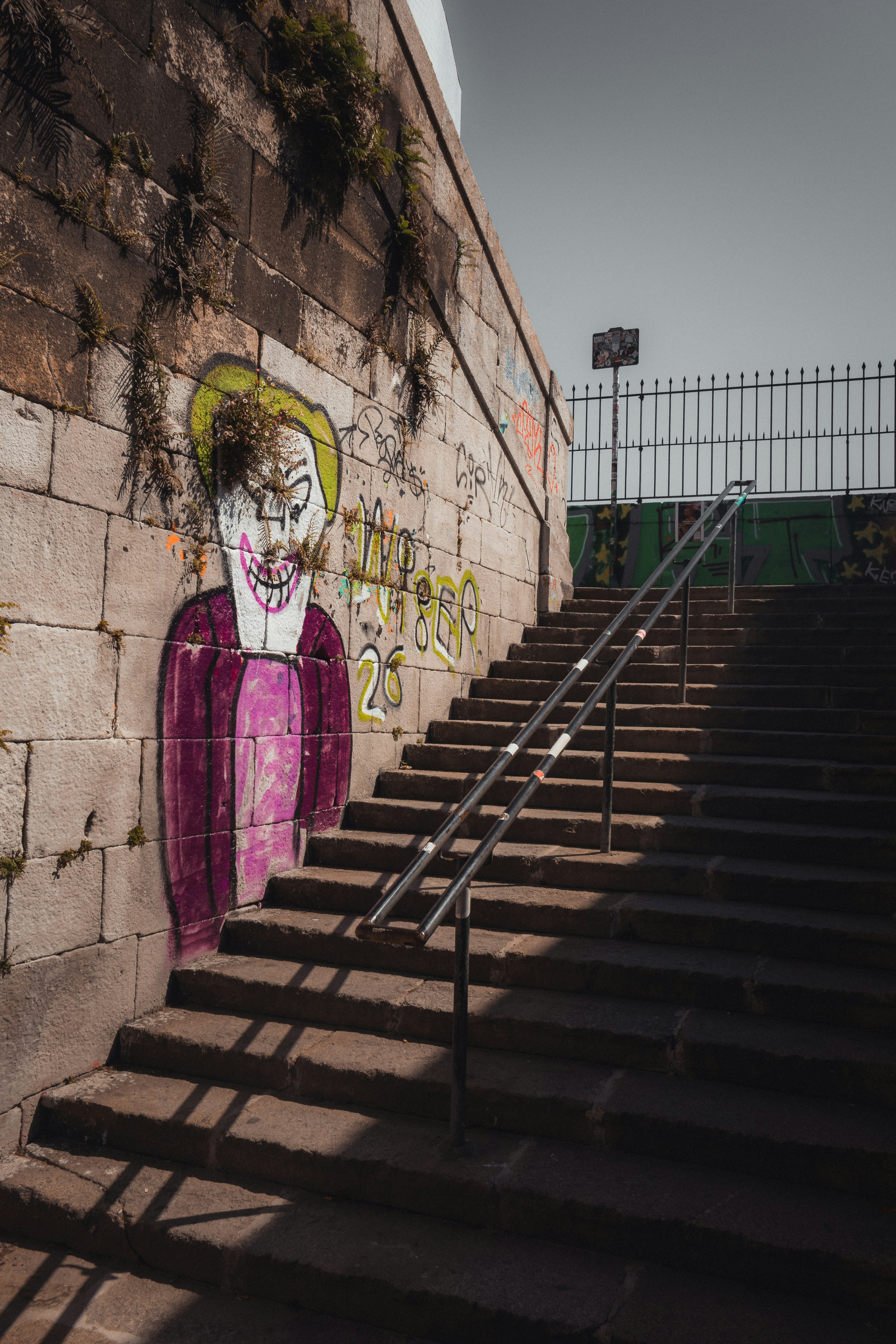 Graffiti of a clown on a stone wall beside stairs.