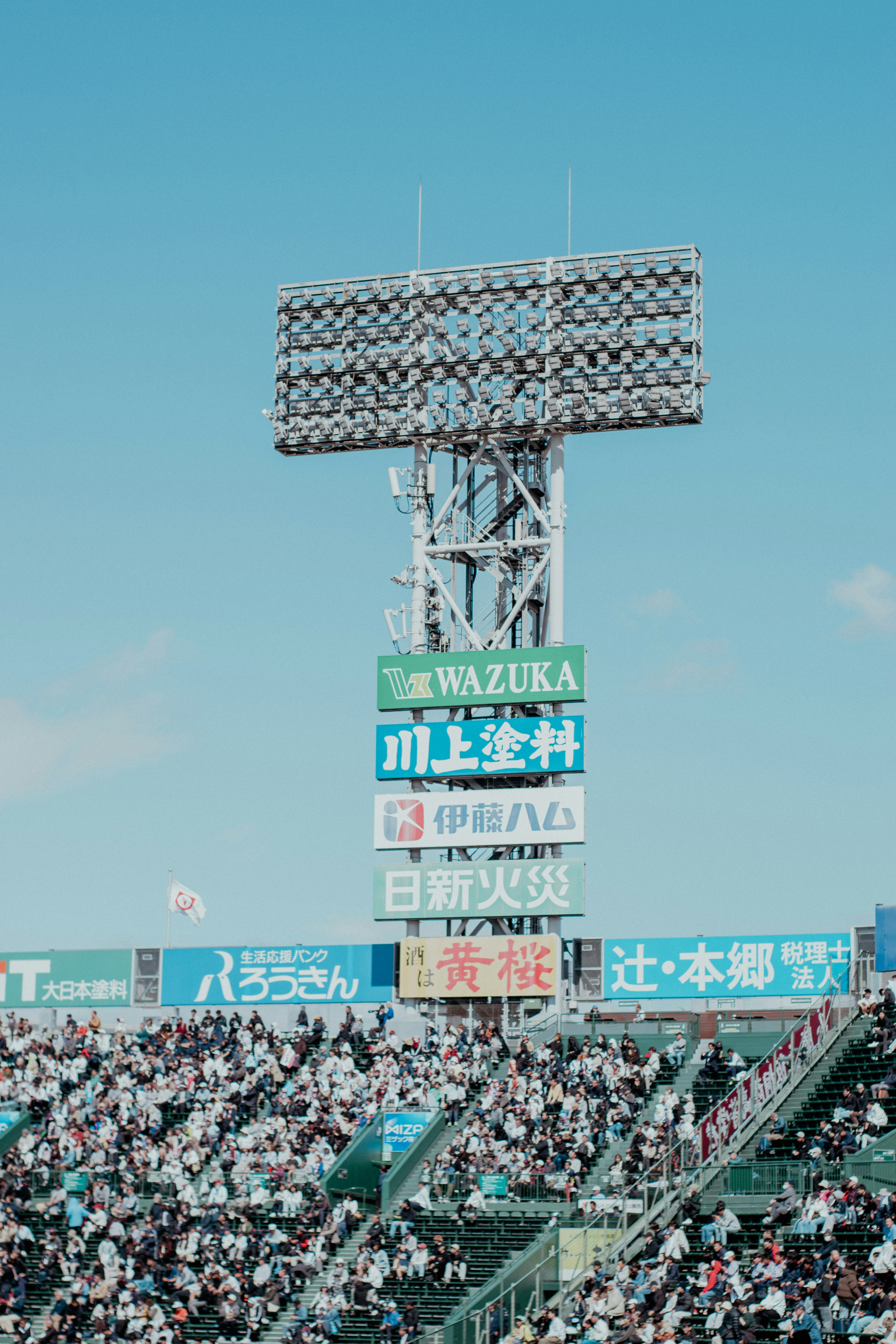 Stadium floodlights tower over cheering crowd under blue sky