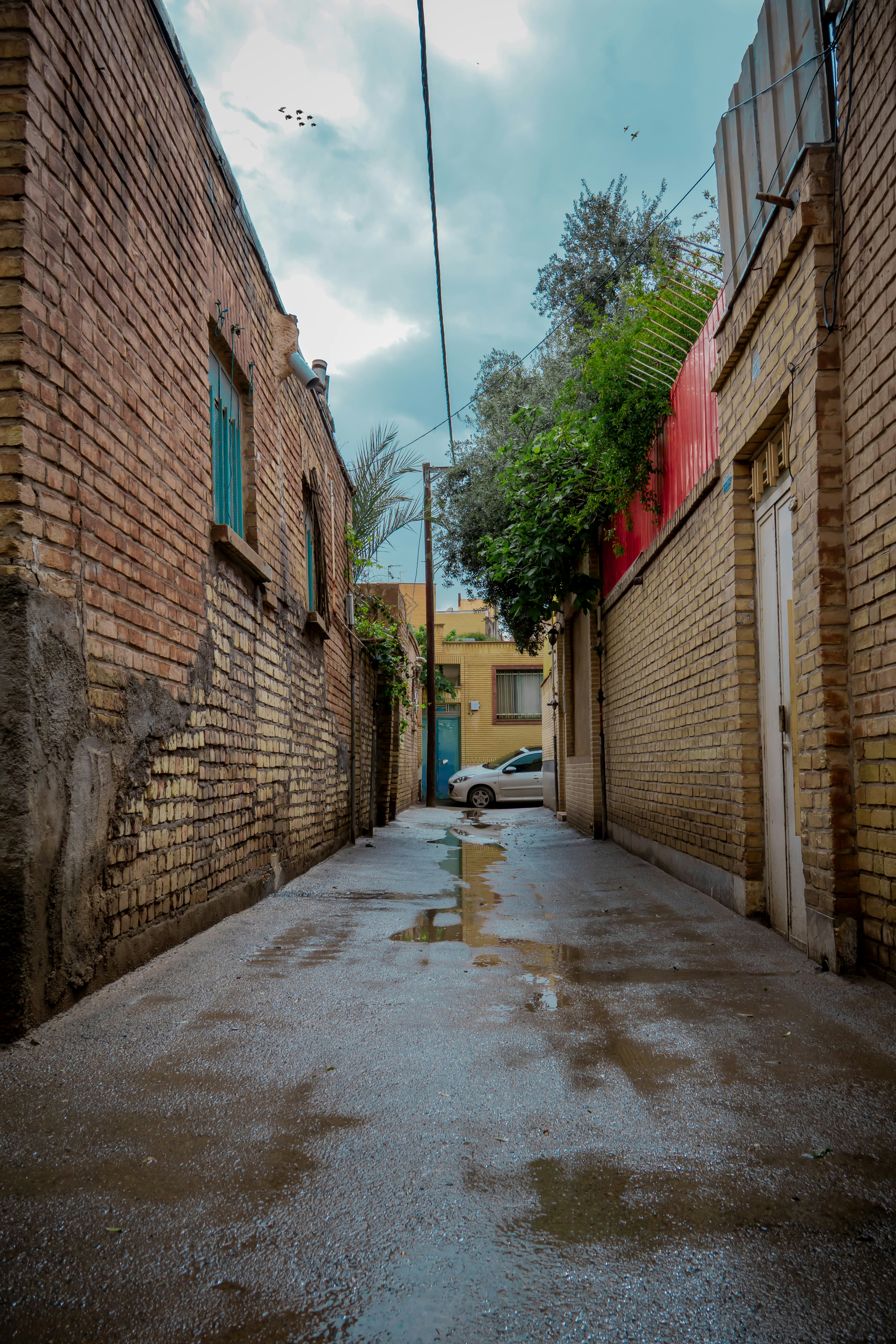 Wet alleyway with brick buildings and a car.