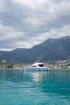 A white yacht floats on turquoise water near mountains.