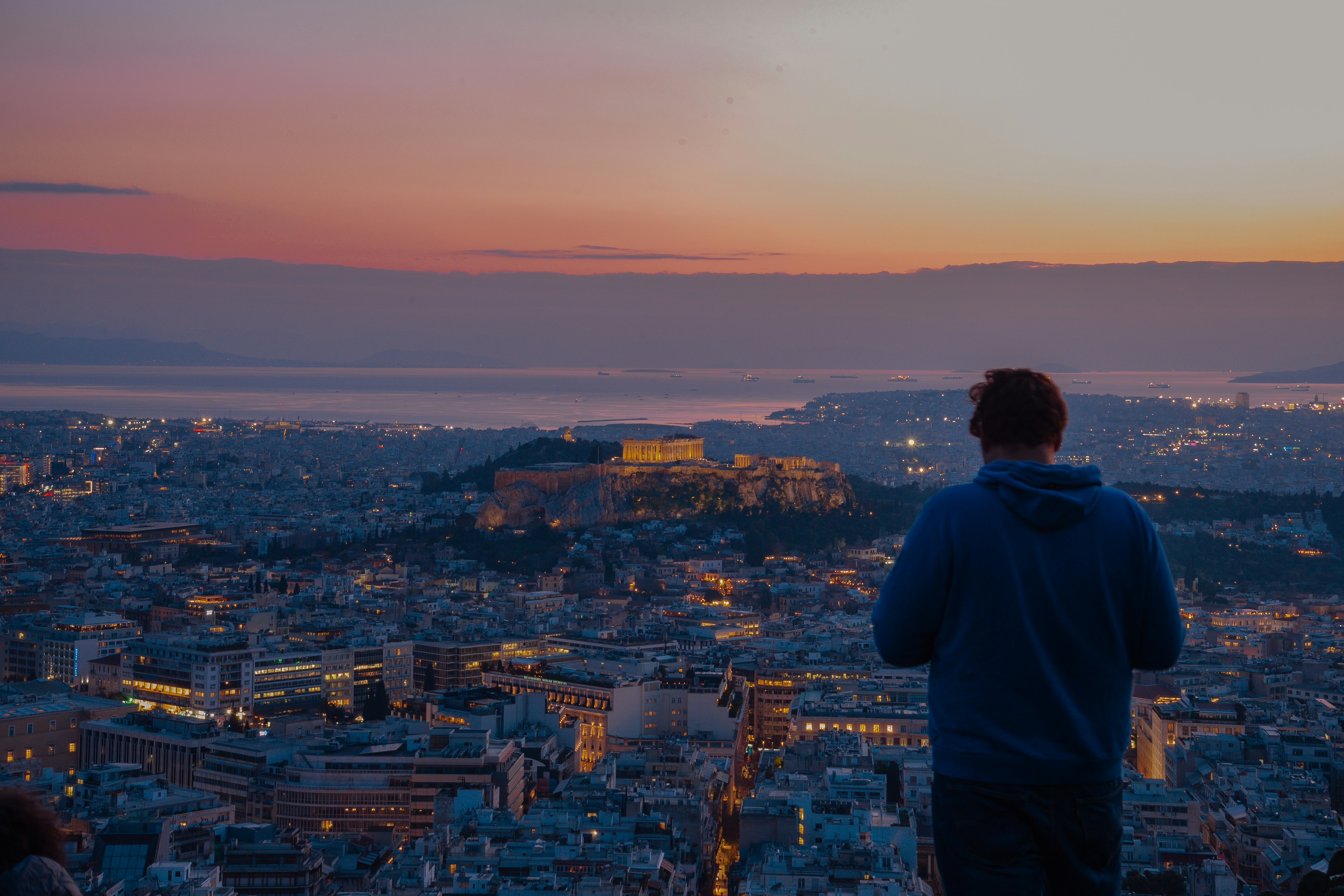 Man watching city lights at dusk from a hilltop