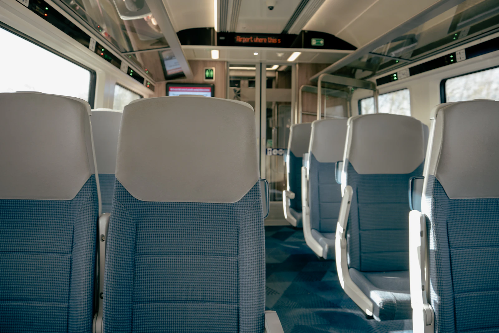 An empty train carriage in daylight, rows of seats and bright windows