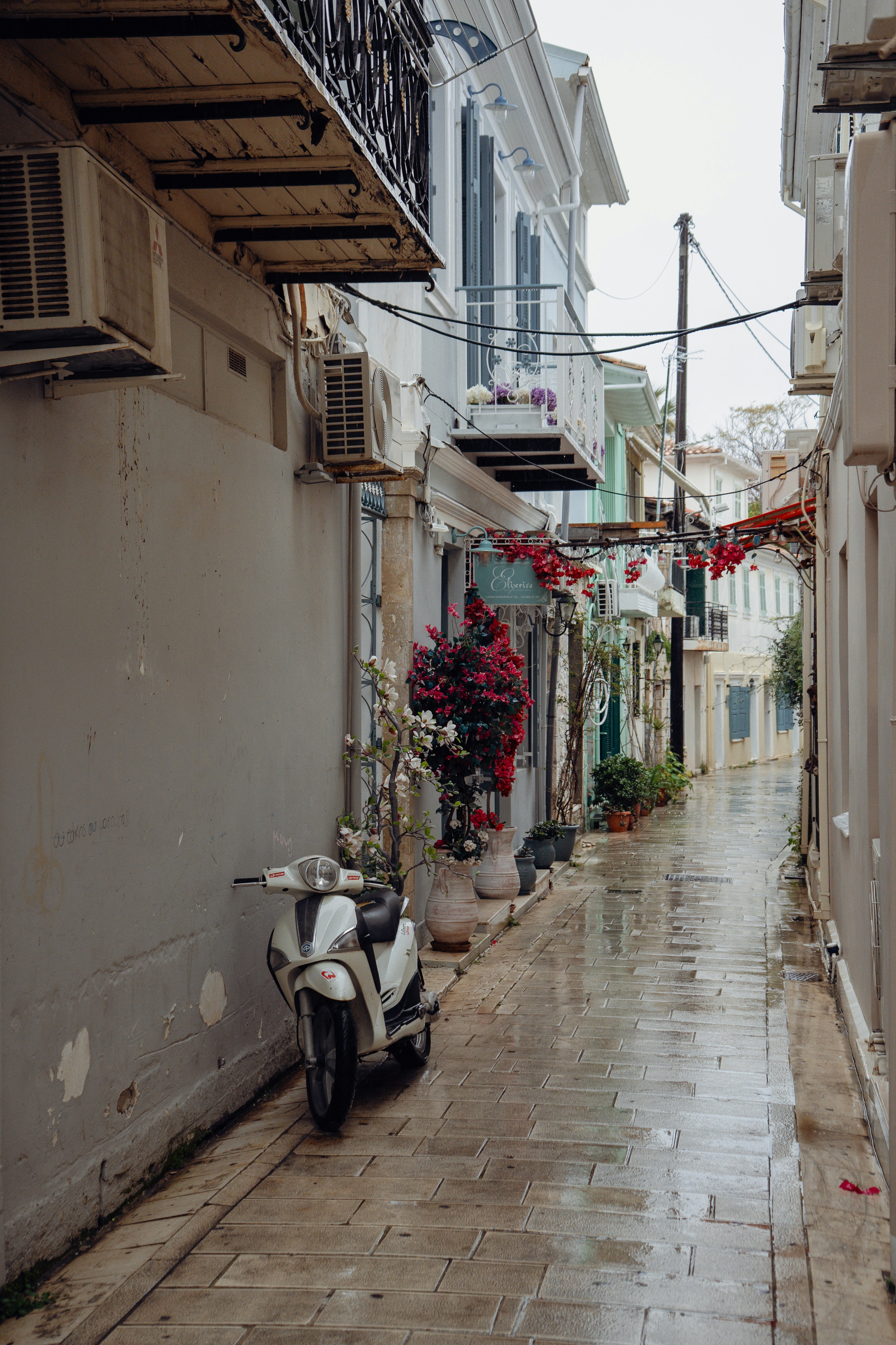 Un scooter blanc garé dans une ruelle pavée et mouillée.