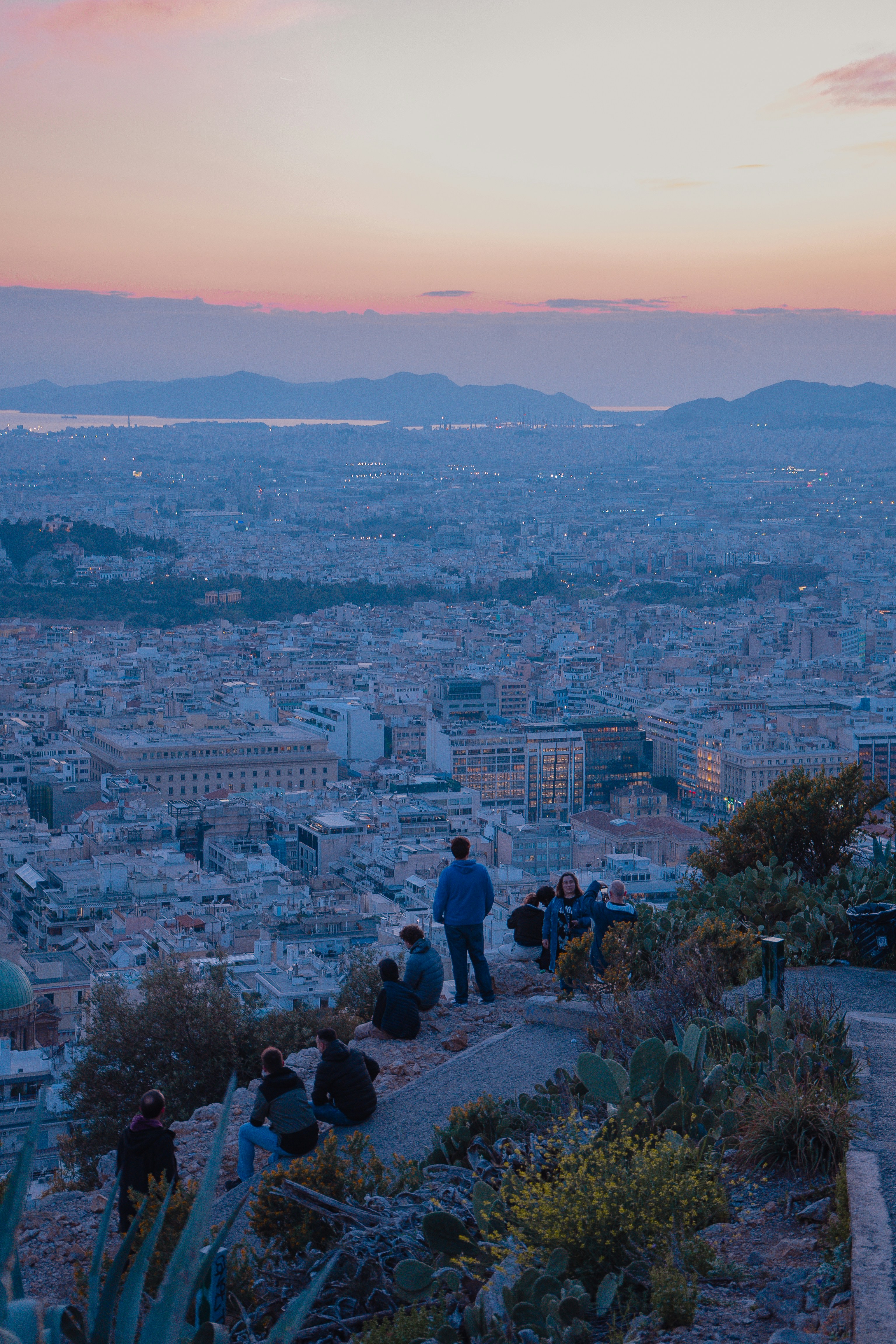 Des gens regardant le coucher de soleil sur une ville tentaculaire depuis un sommet de colline.