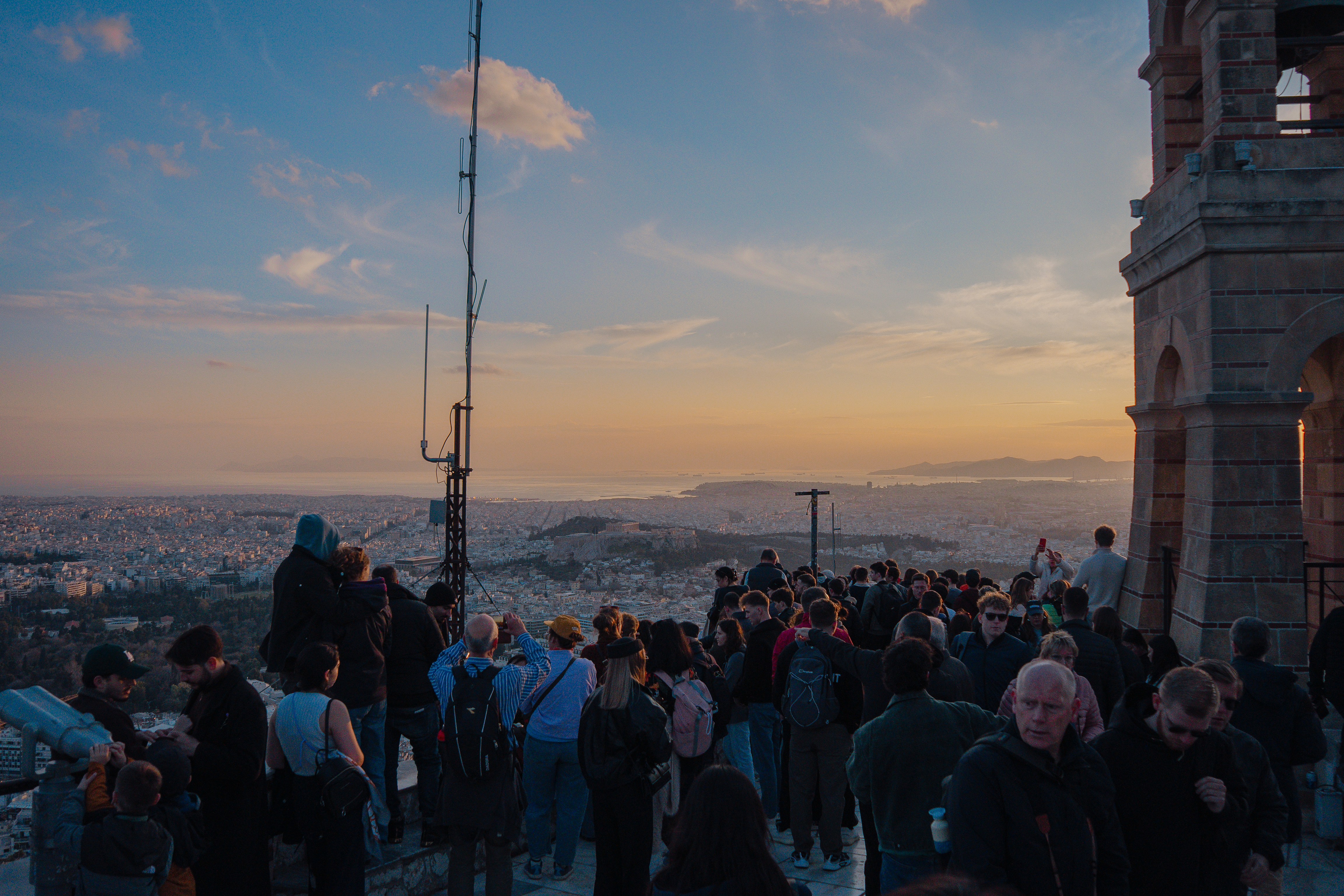 Crowd watches sunset over city from hilltop tower viewpoint