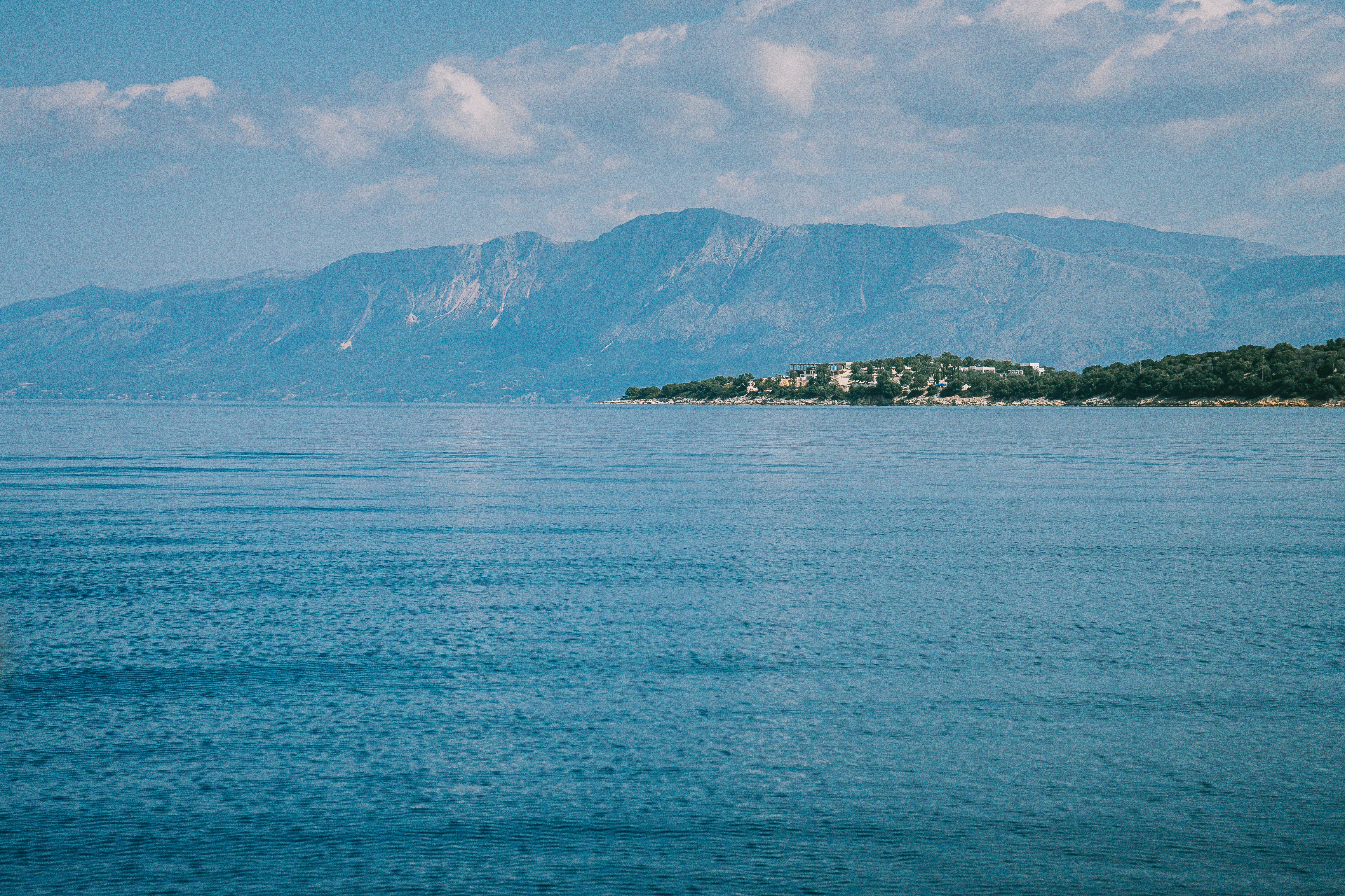 Une eau d’océan bleue calme avec des montagnes et un littoral lointains.
