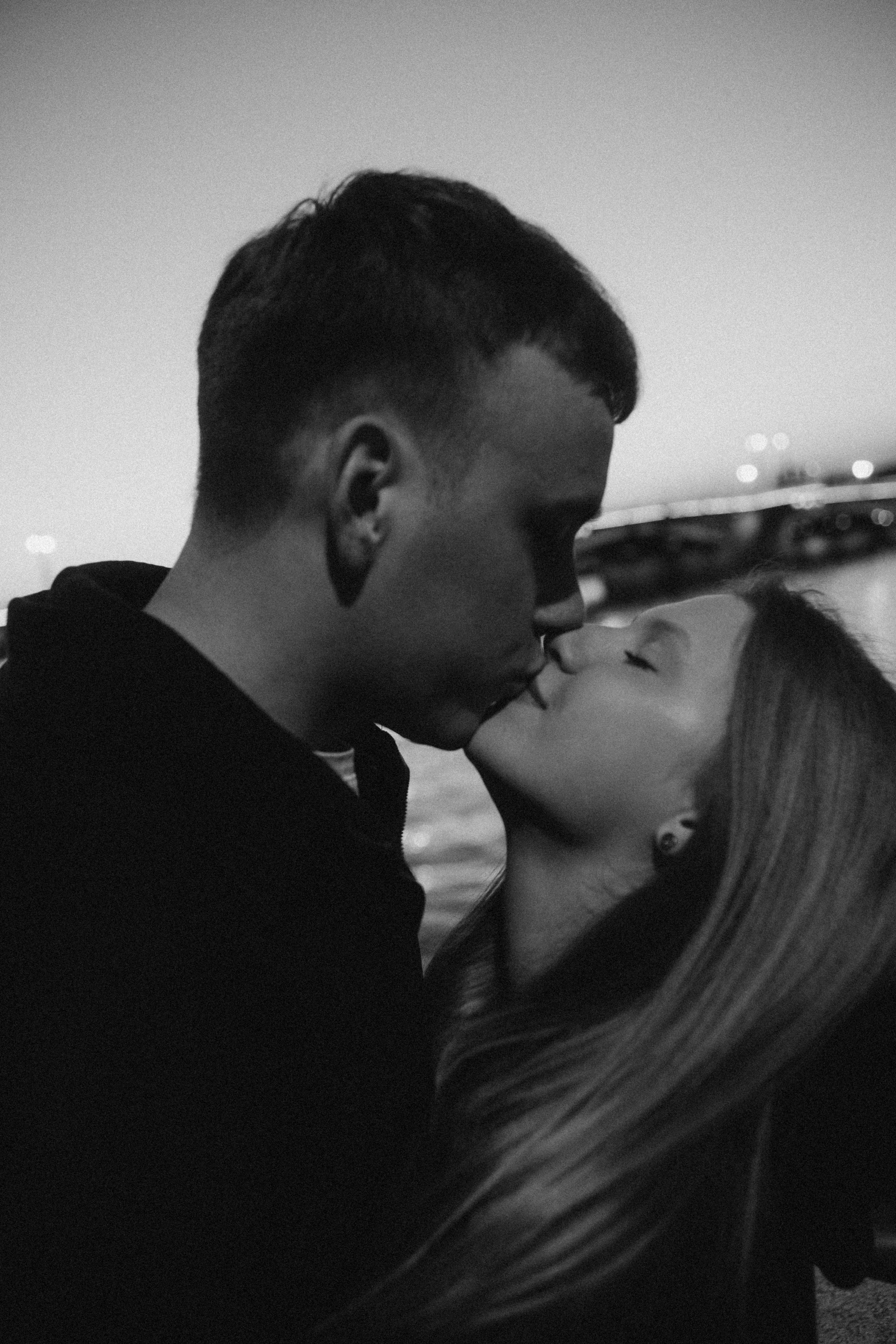 Una pareja besándose al anochecer con las luces de la ciudad borrosas de fondo