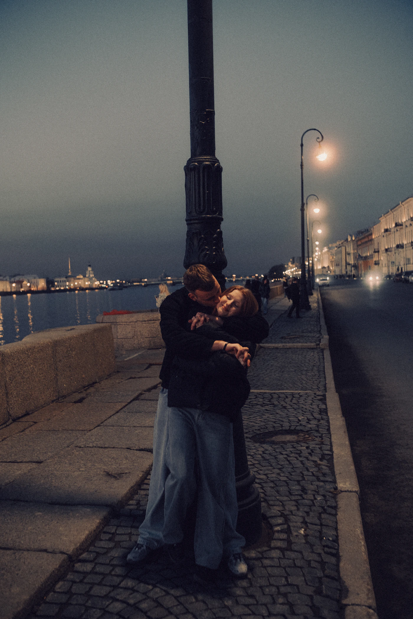 Couple embracing romantically beside a vintage iron lamppost on a cobblestone street at night with warm street light