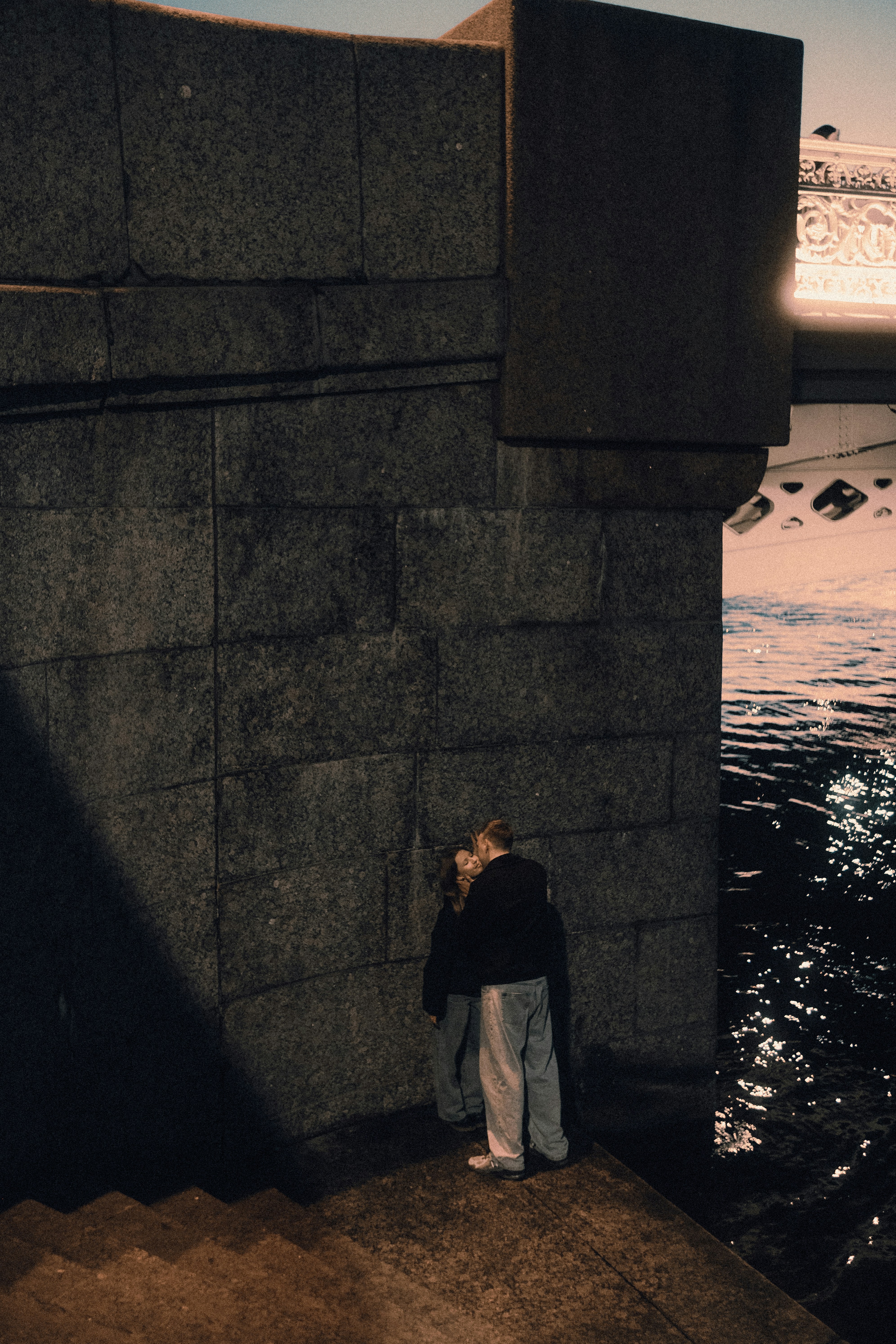 夜、水辺の石壁のそばでキスをするカップル