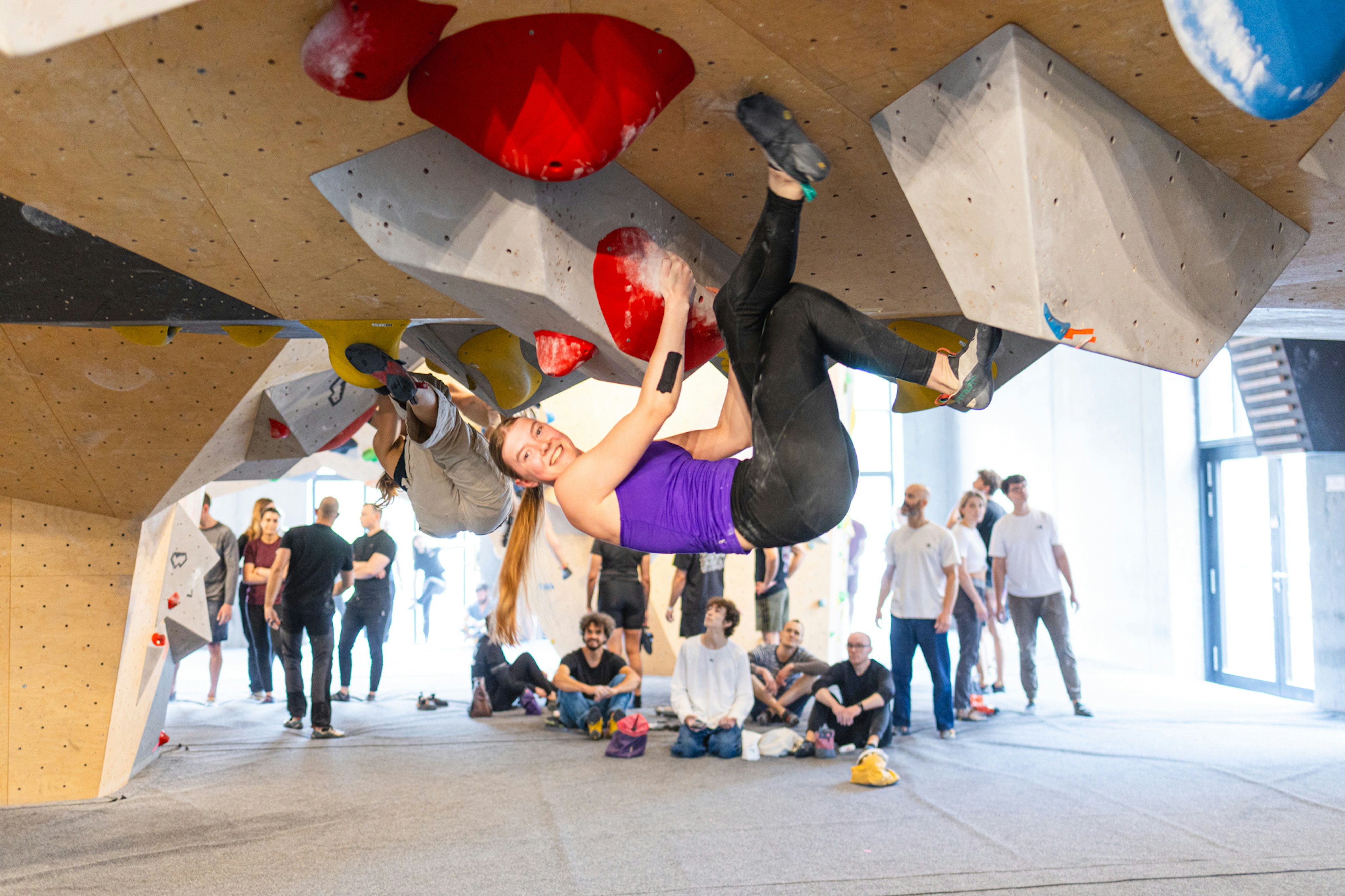 Woman bouldering indoors with people watching