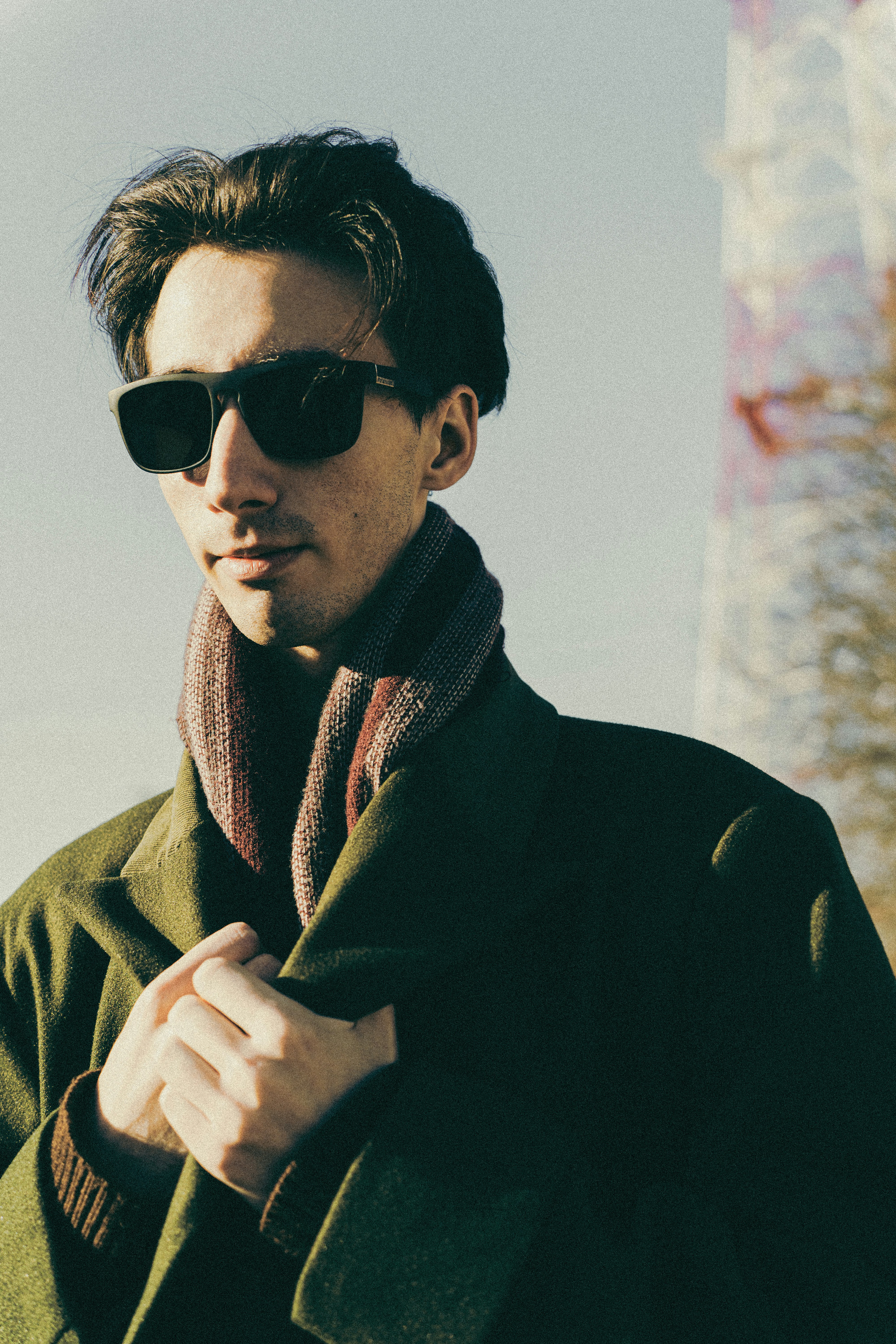 Homme portant des lunettes de soleil, une écharpe et un manteau dehors.