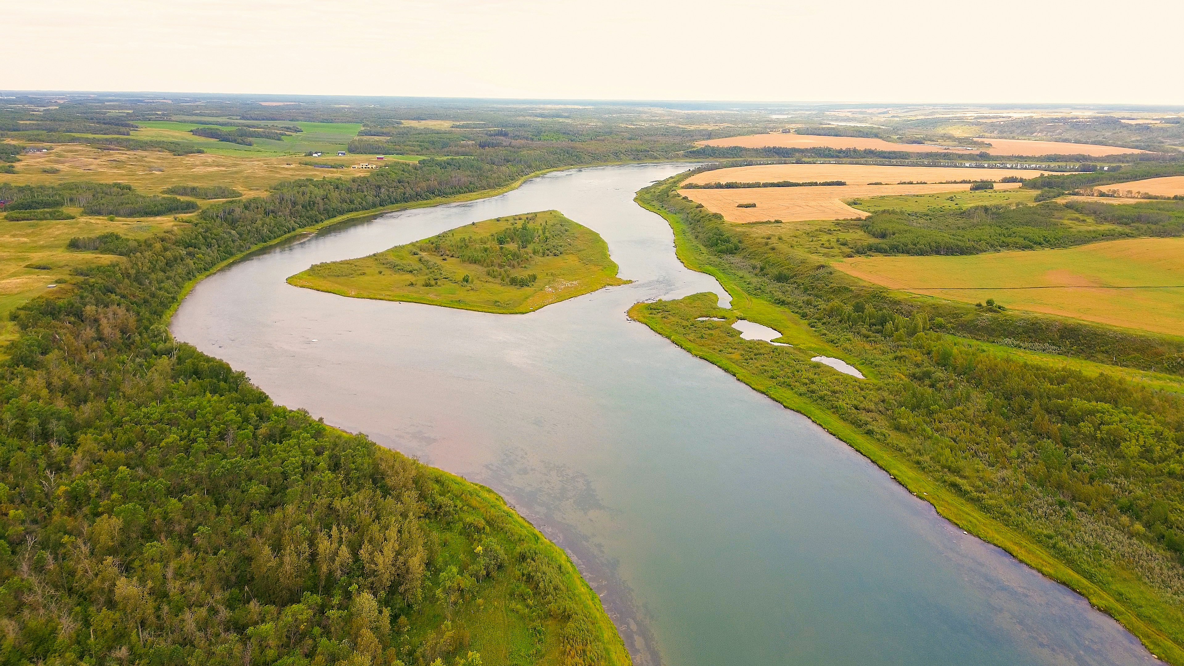 Ein breiter Fluss schlängelt sich durch grüne Felder und Wälder.