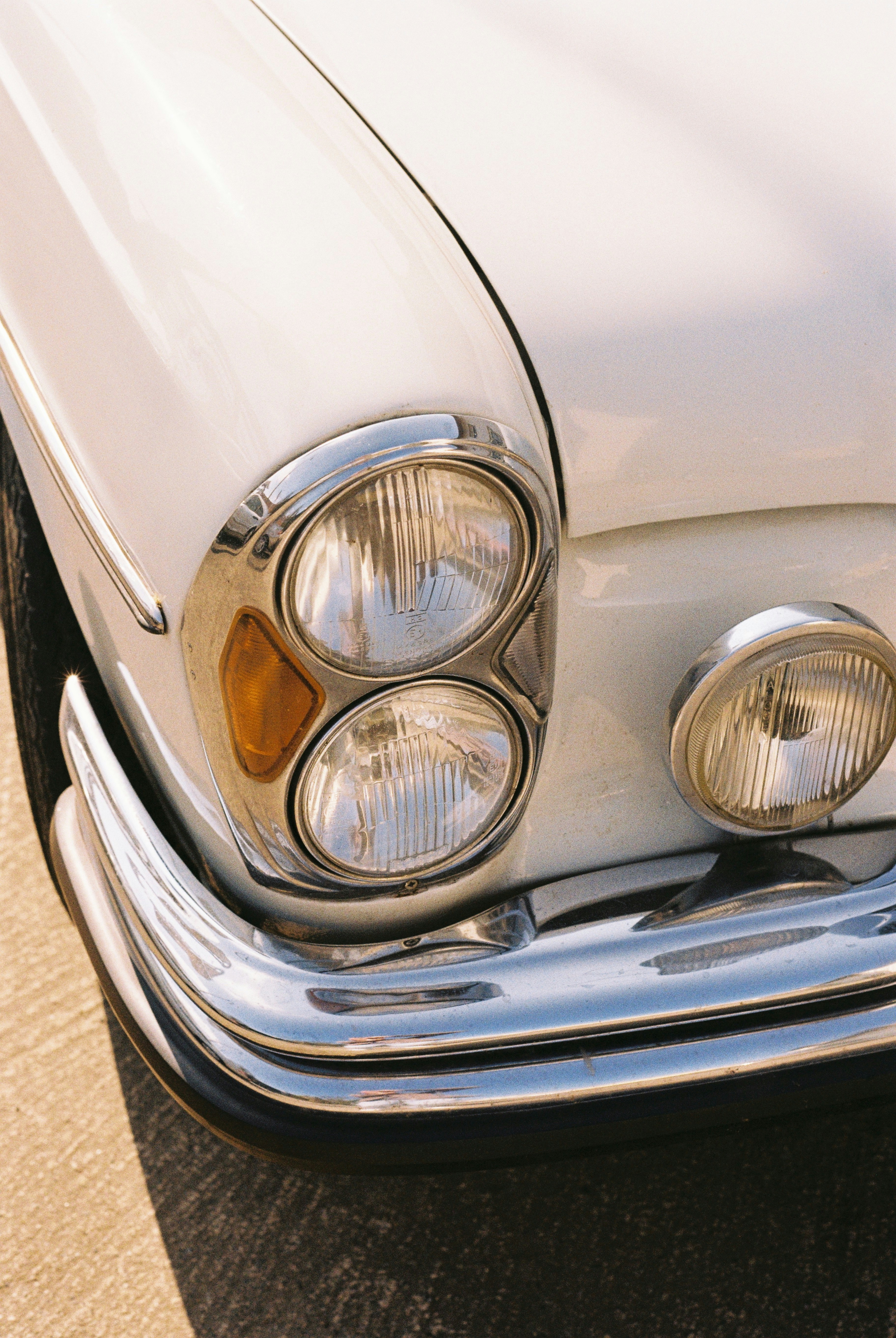 Close-up of a vintage white car's headlights and chrome bumper.