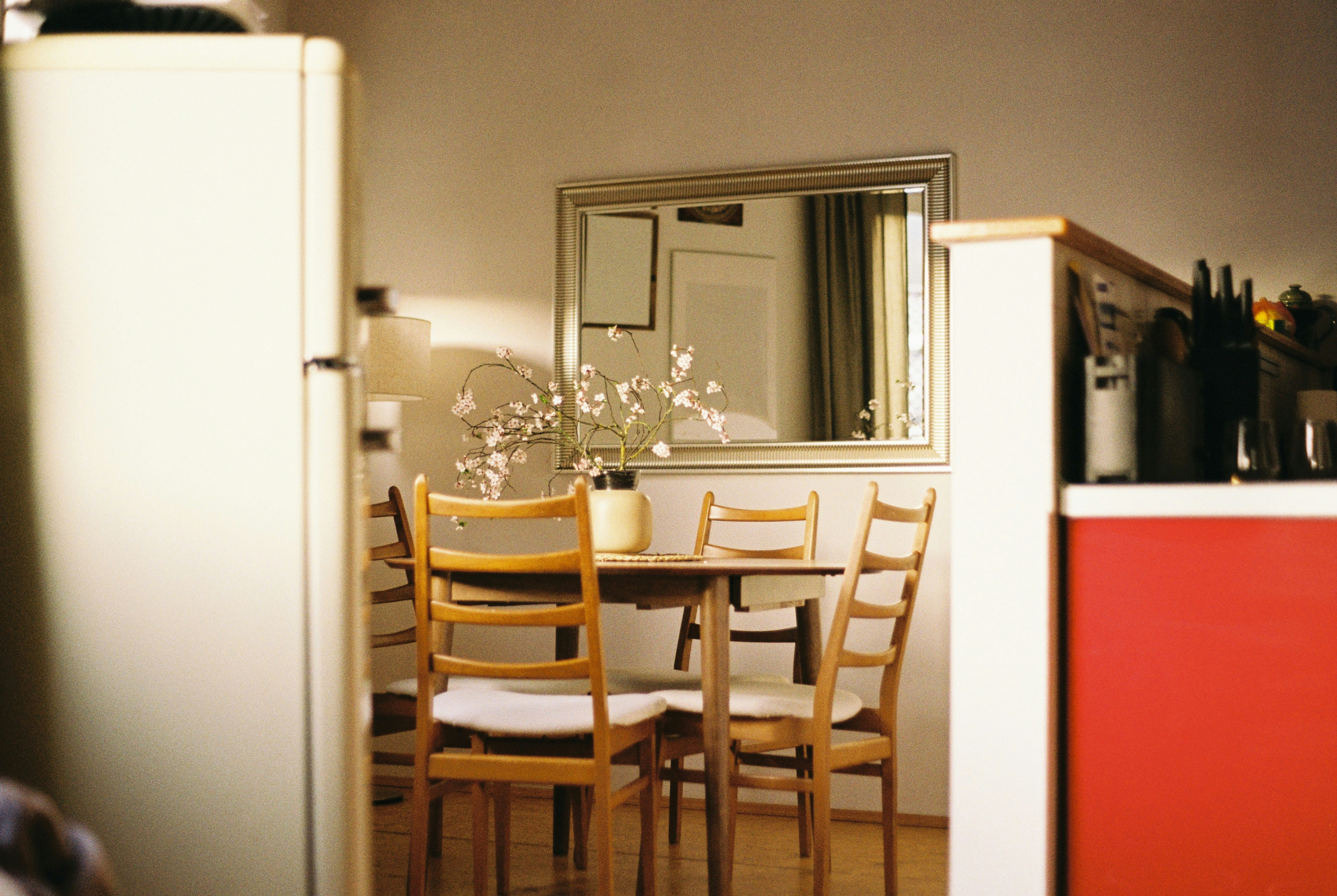 A dining table with four chairs and a refrigerator.