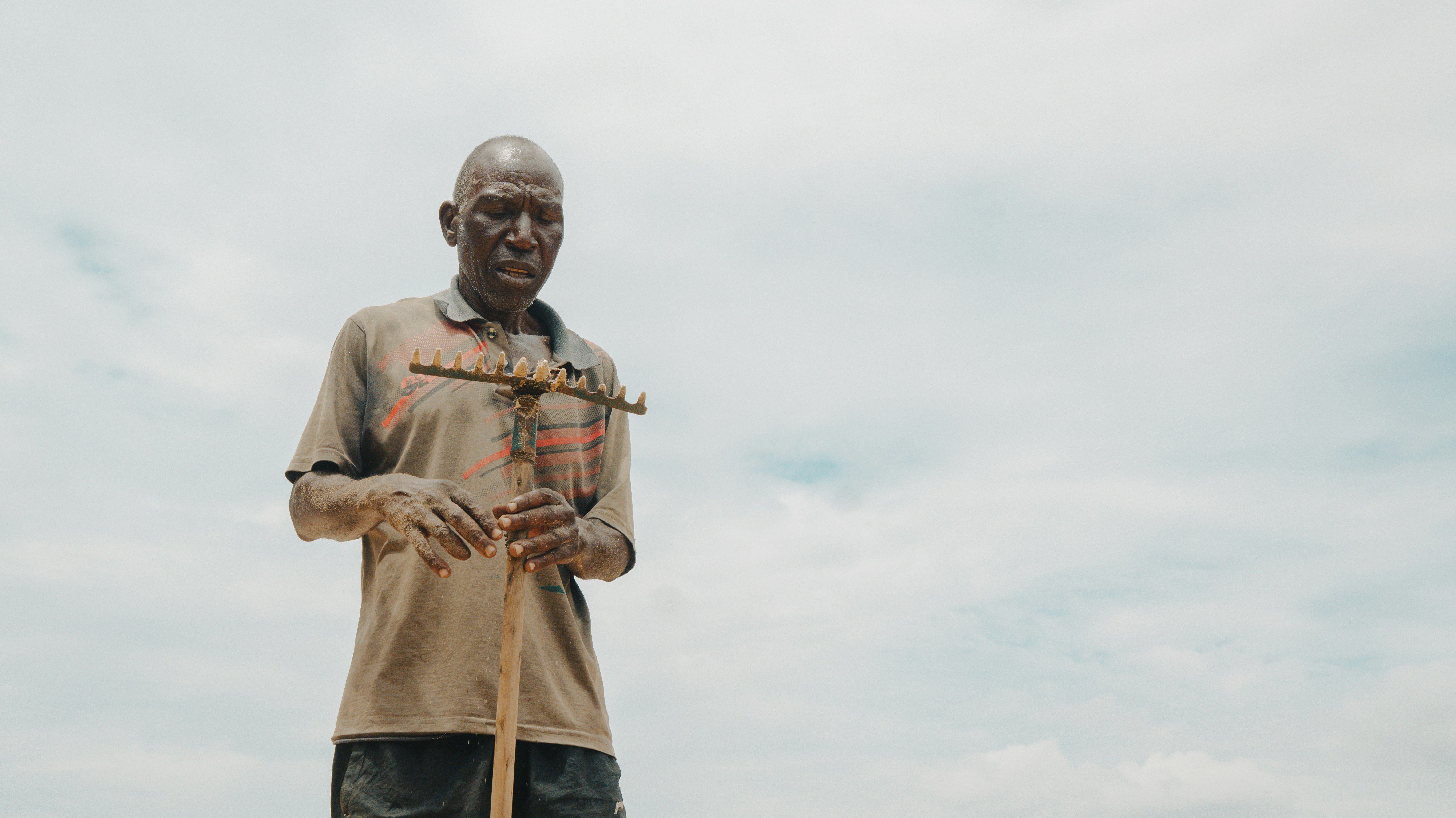 An elderly man stands against a cloudy sky.