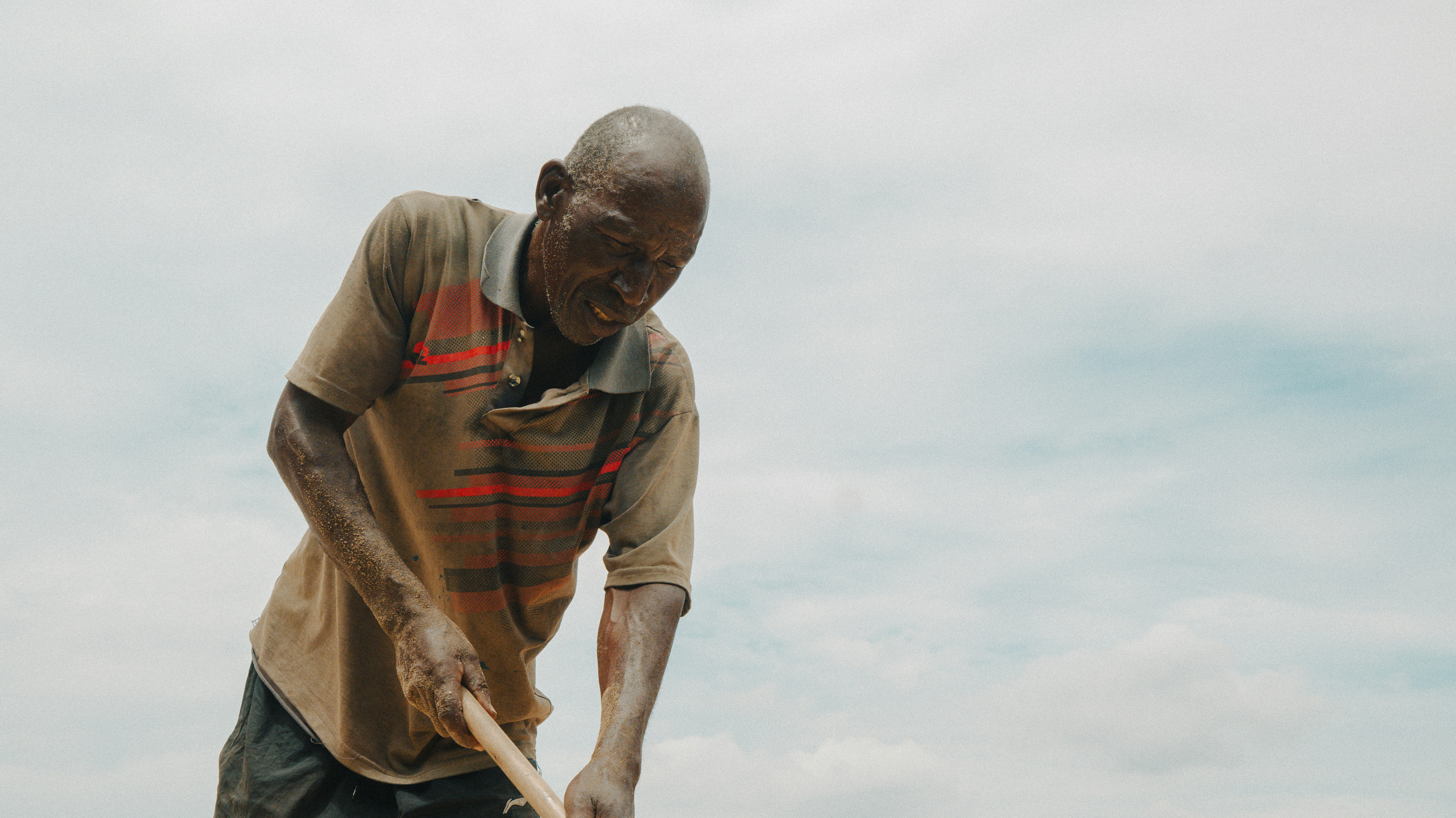 An elderly man digging with a shovel outdoors.