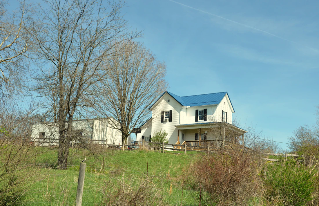 White farmhouse with a blue roof on an open lot