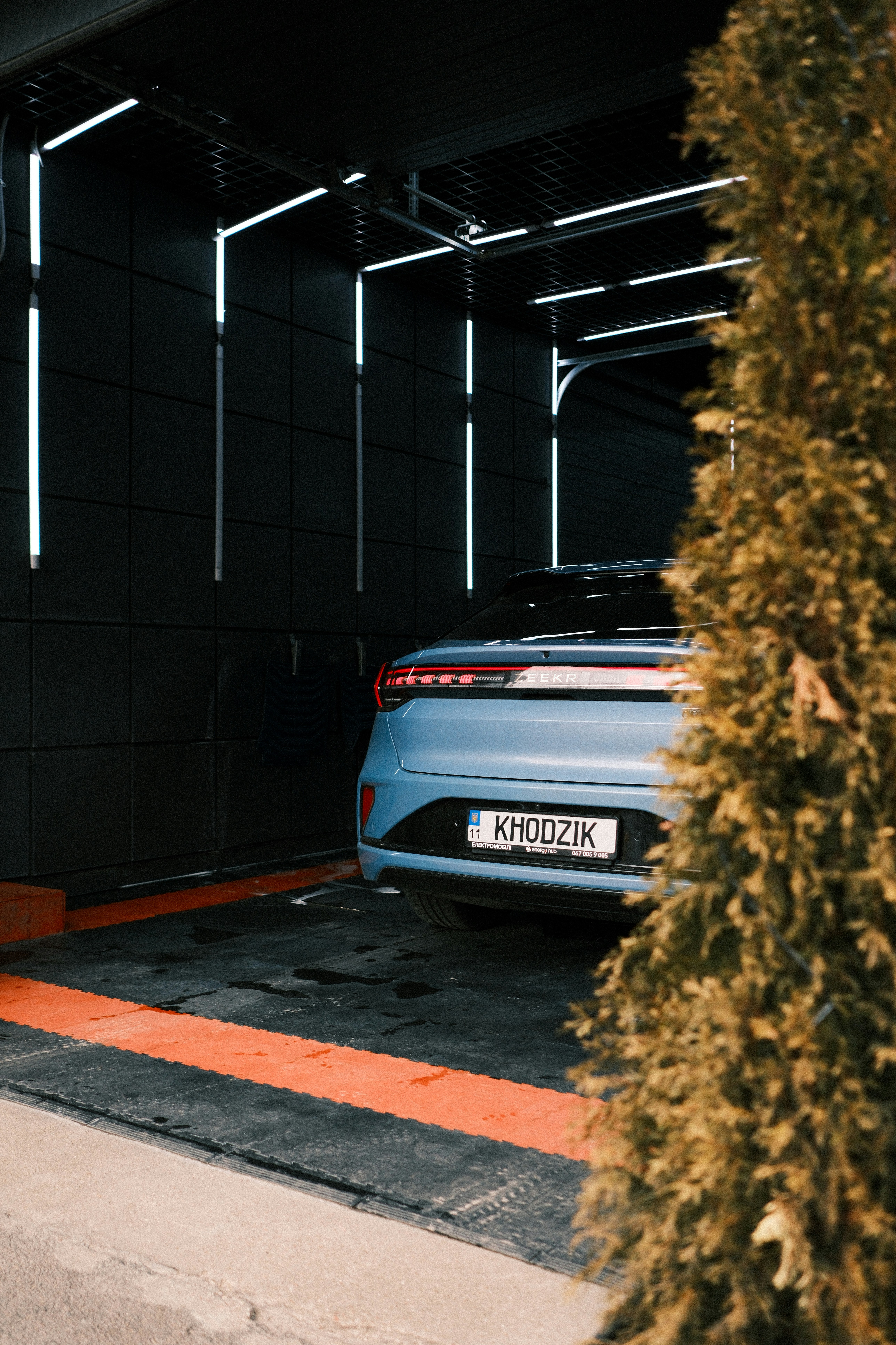 Blue car parked in a modern garage with neon lights.