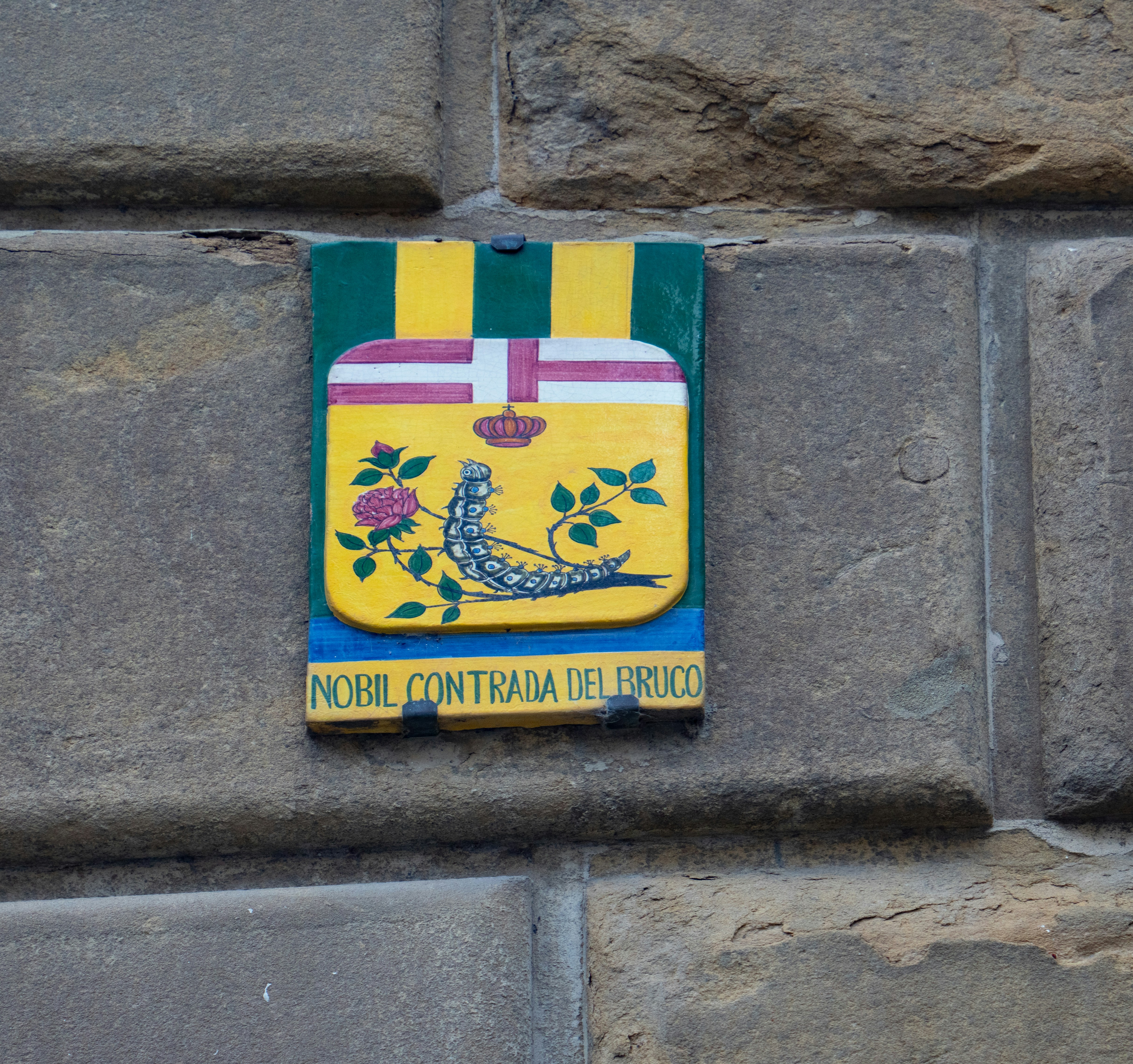 Coat of arms with caterpillar and rose on stone wall.
