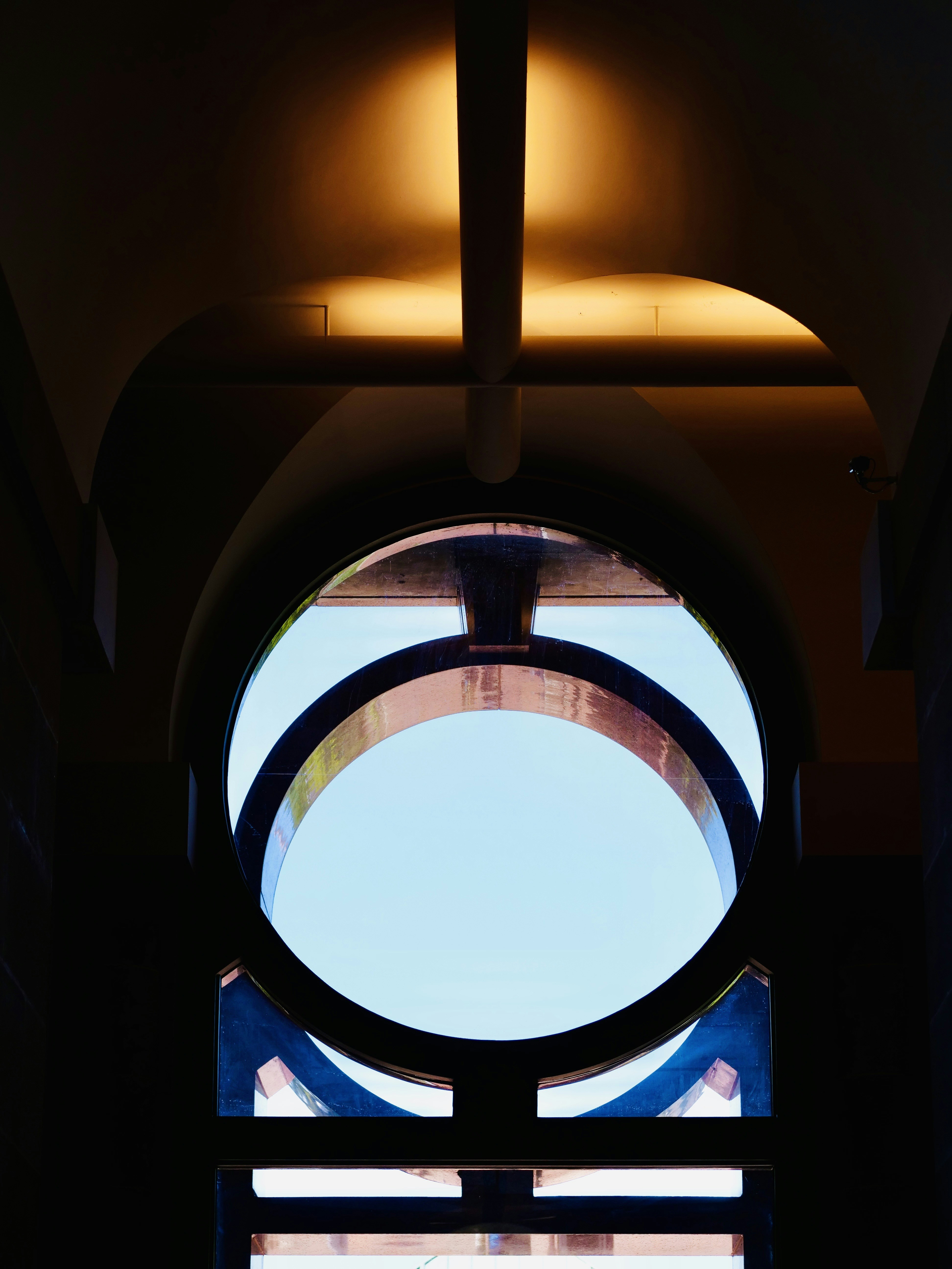 明るい空と建築の細部が描かれた円形の窓