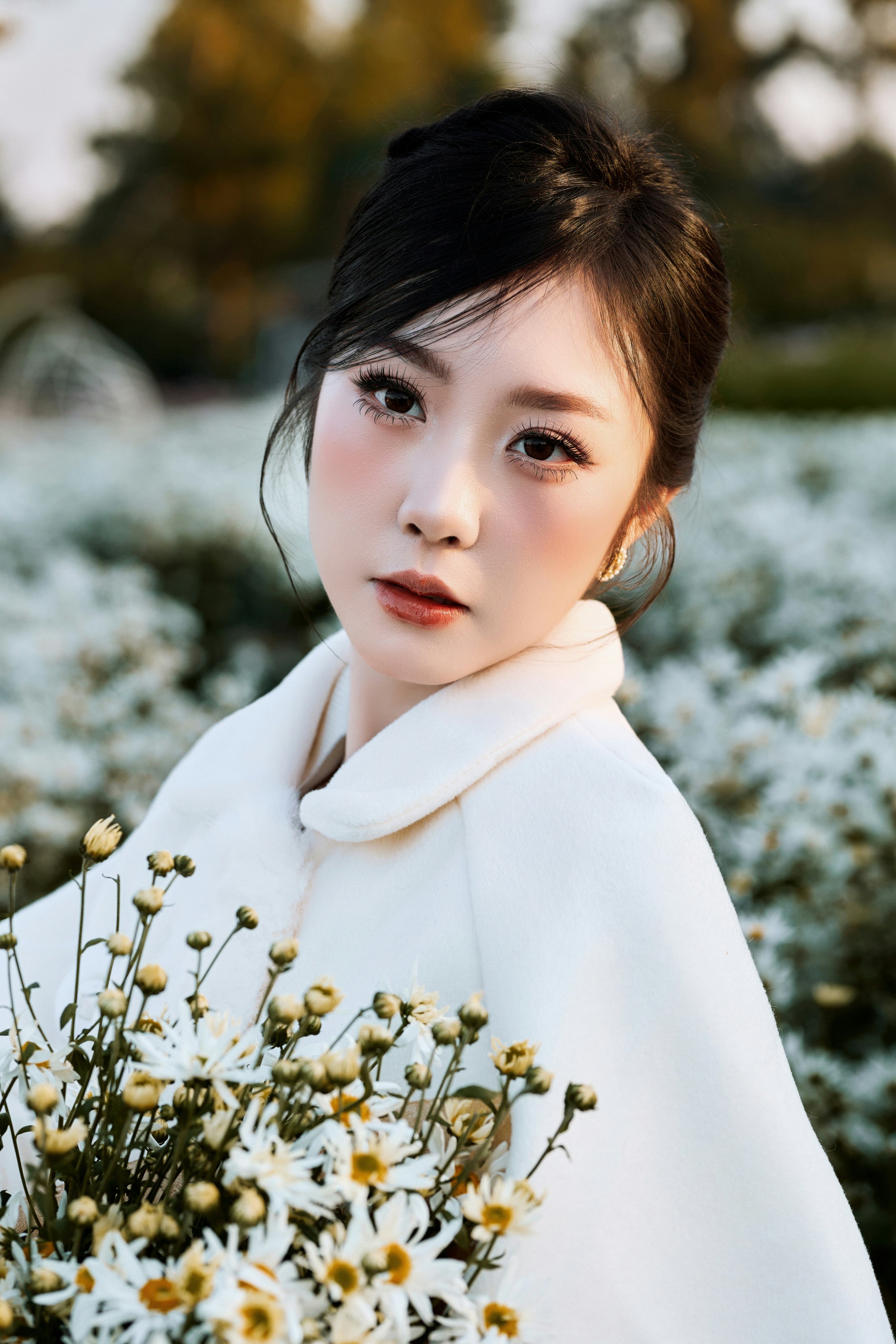 Young woman in white coat holding white flowers outdoors