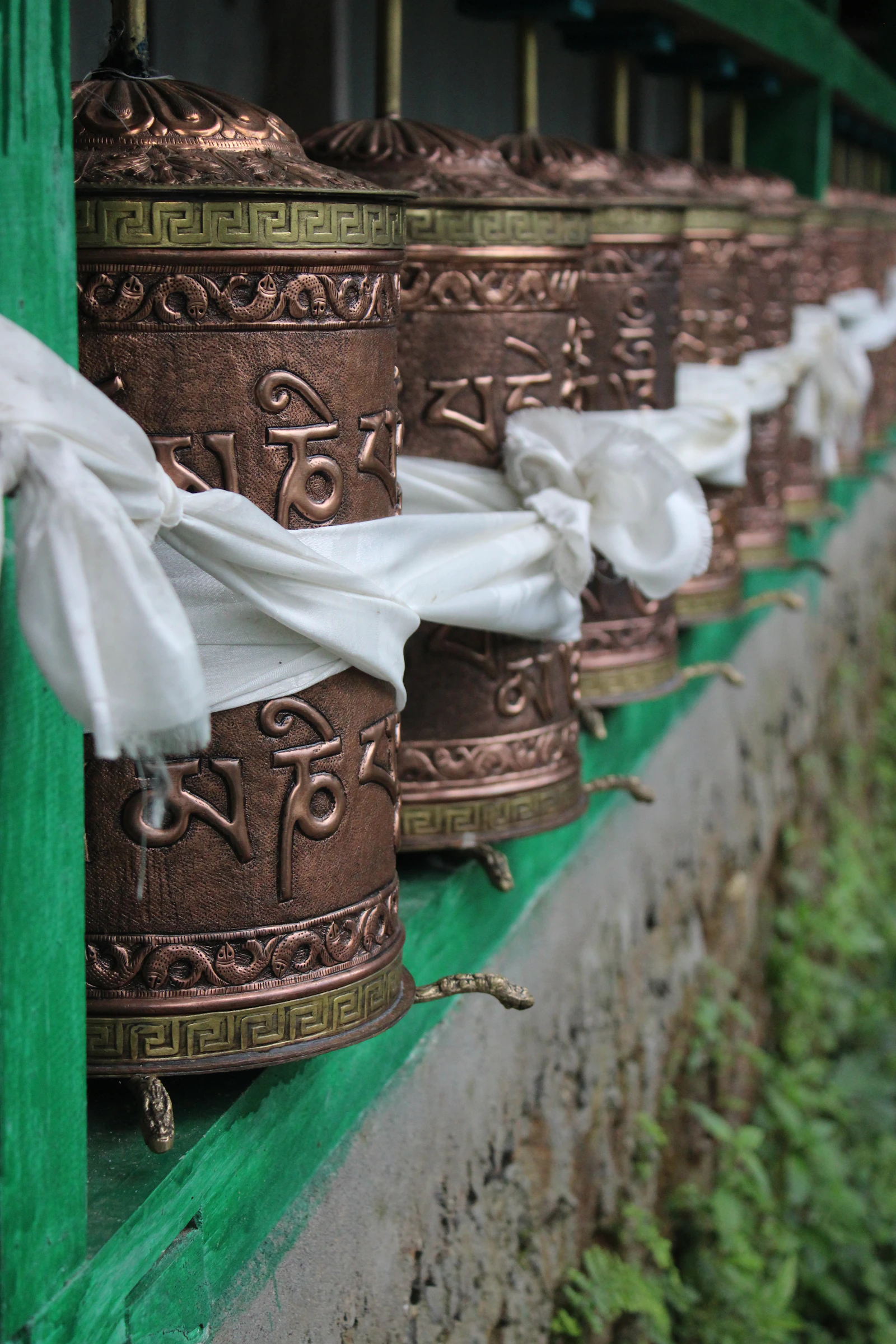 Copper prayer wheels tied with white khadas at a Buddhist shrine in Ravangla, South Sikkim